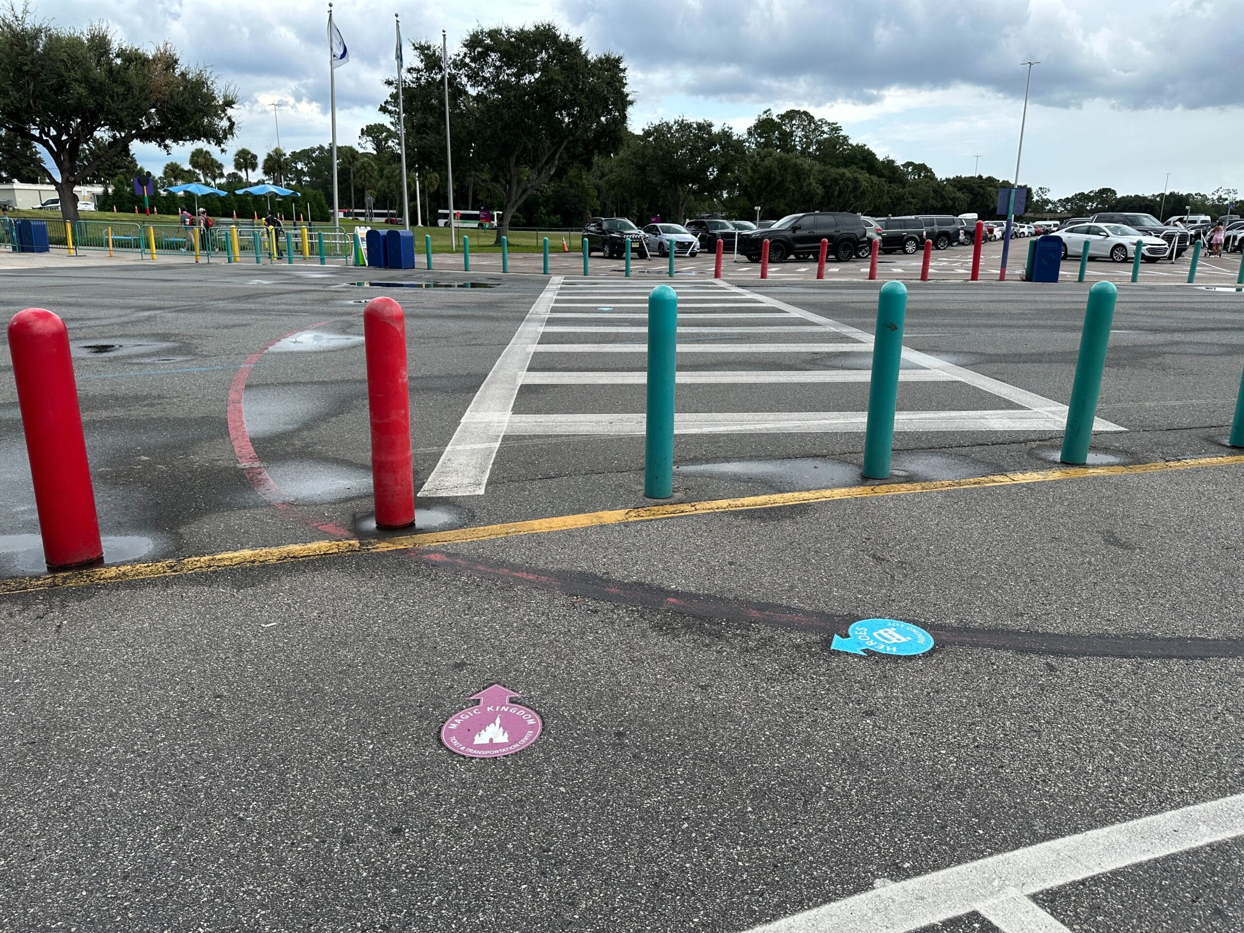 A crosswalk with red and teal posts, Parking Lot Signs, and character-themed directional decals under a cloudy sky.