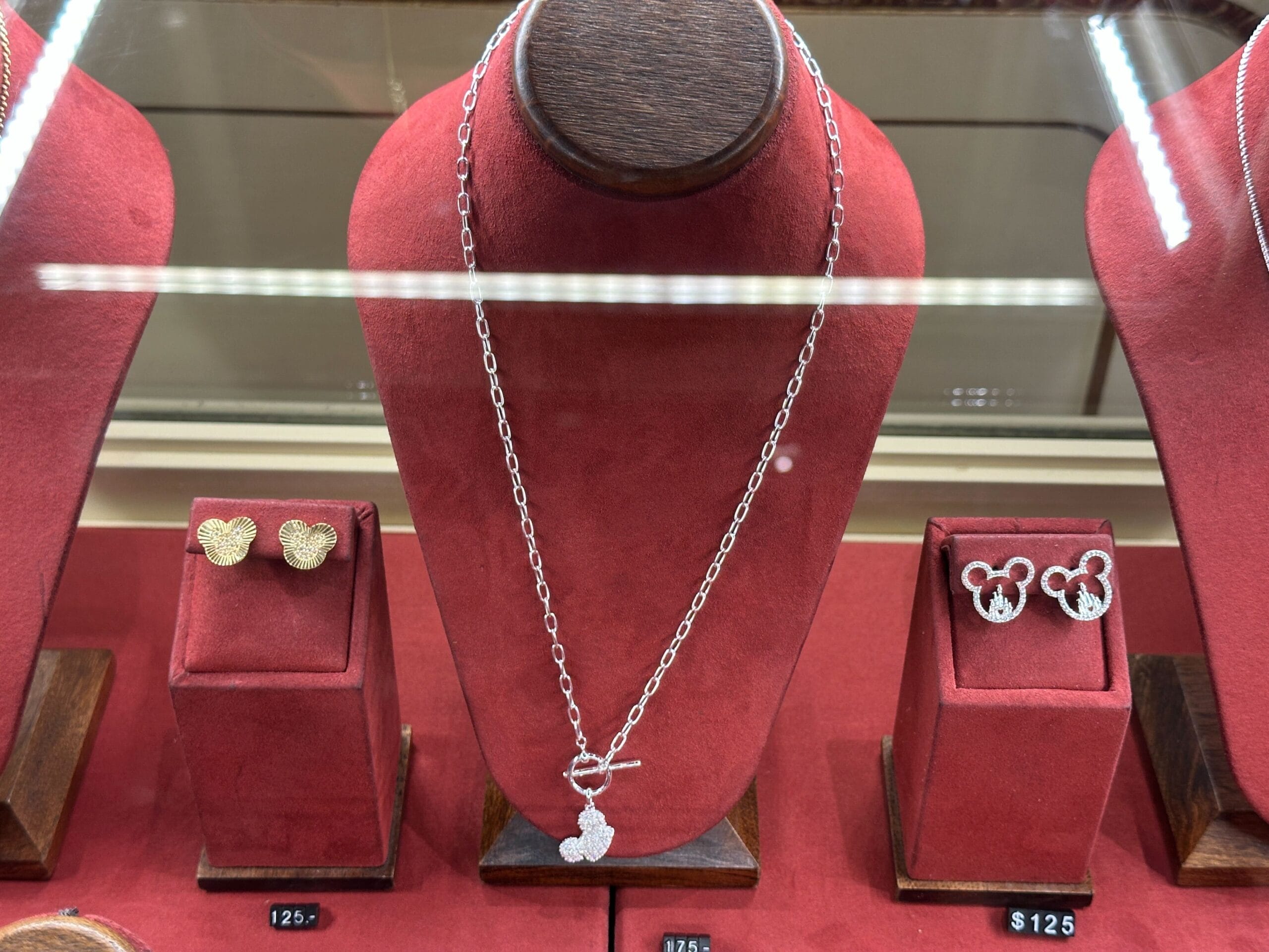 Silver necklace with a Mickey Mouse pendant and matching earrings displayed on red velvet stands in a jewelry case.