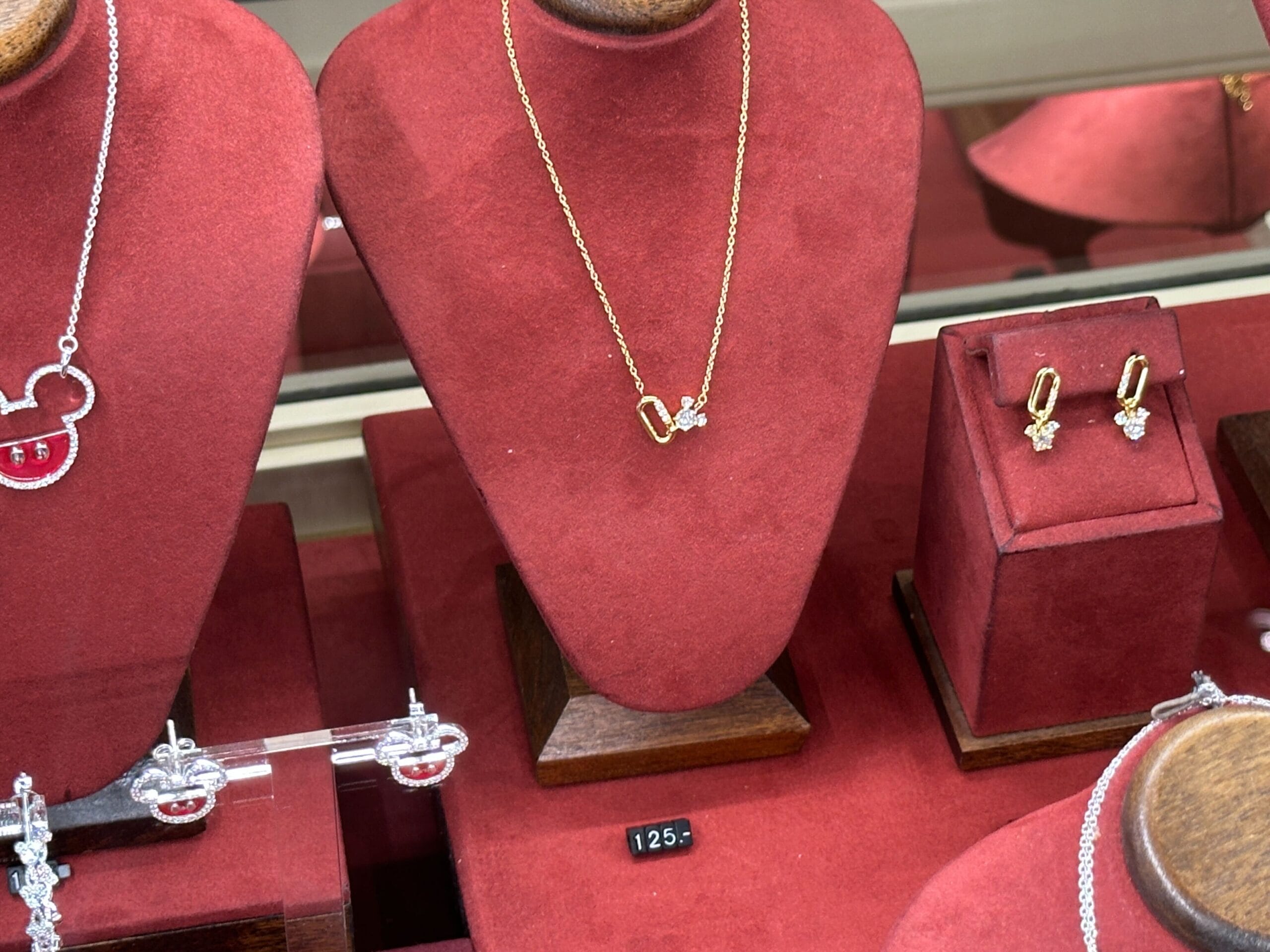 Gold necklace and matching earrings with small diamond accents displayed on red velvet stands in a jewelry case.