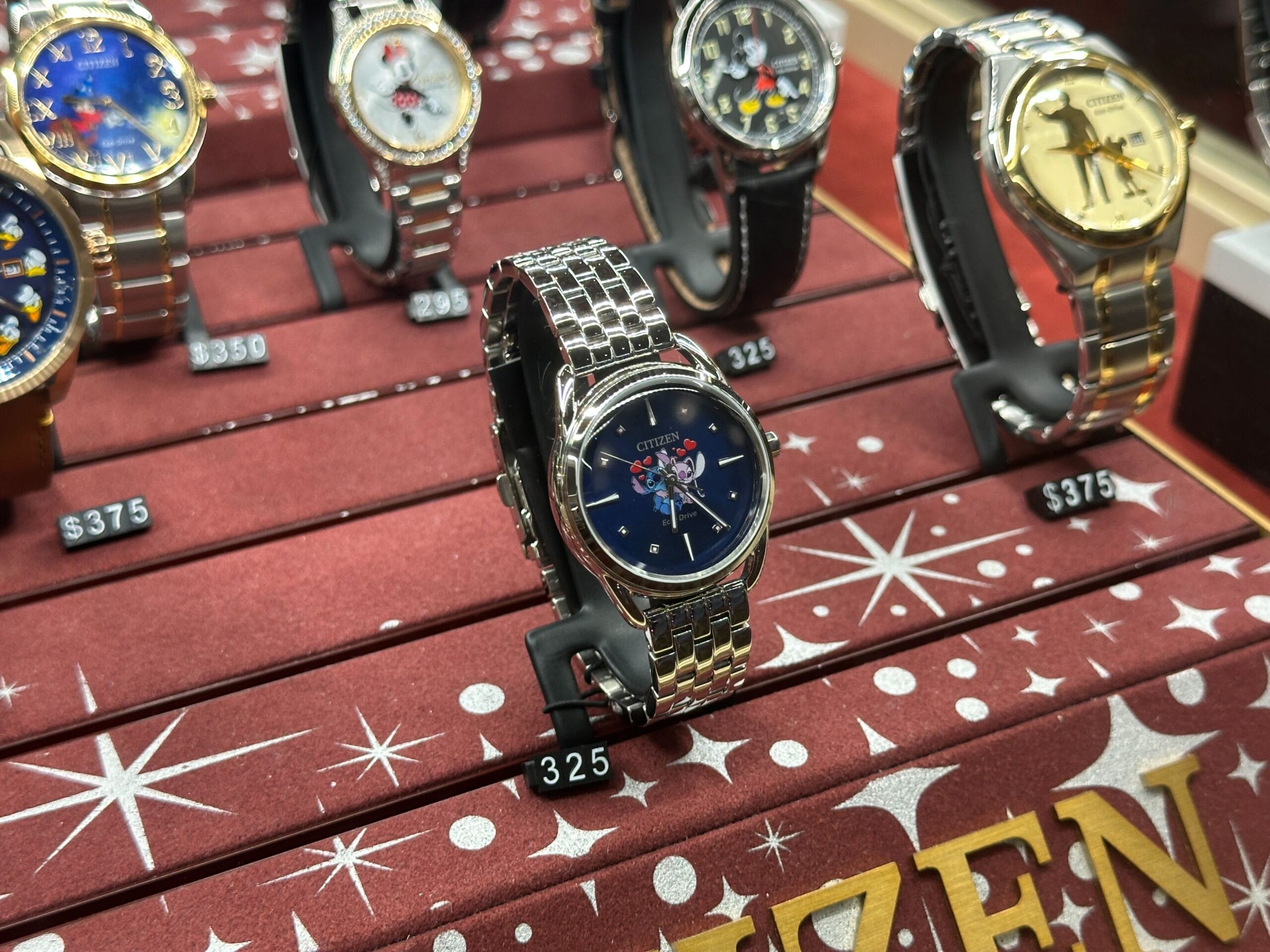 Citizen wristwatch with a silver band on display, priced at $325, among other watches in a store case.