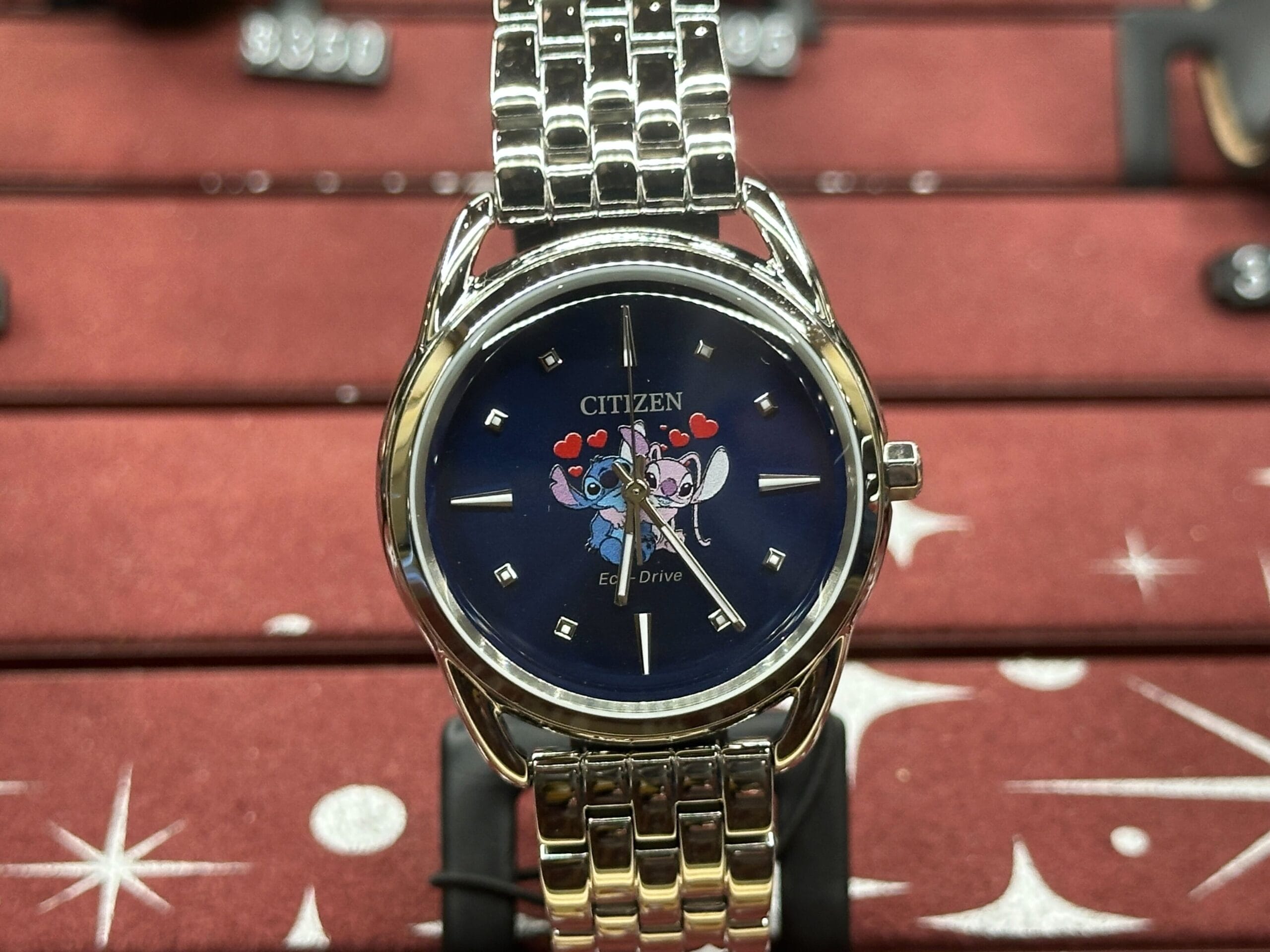 Citizen watch with a blue face featuring cartoon cats with hearts, displayed on a silver metal band against a red background.