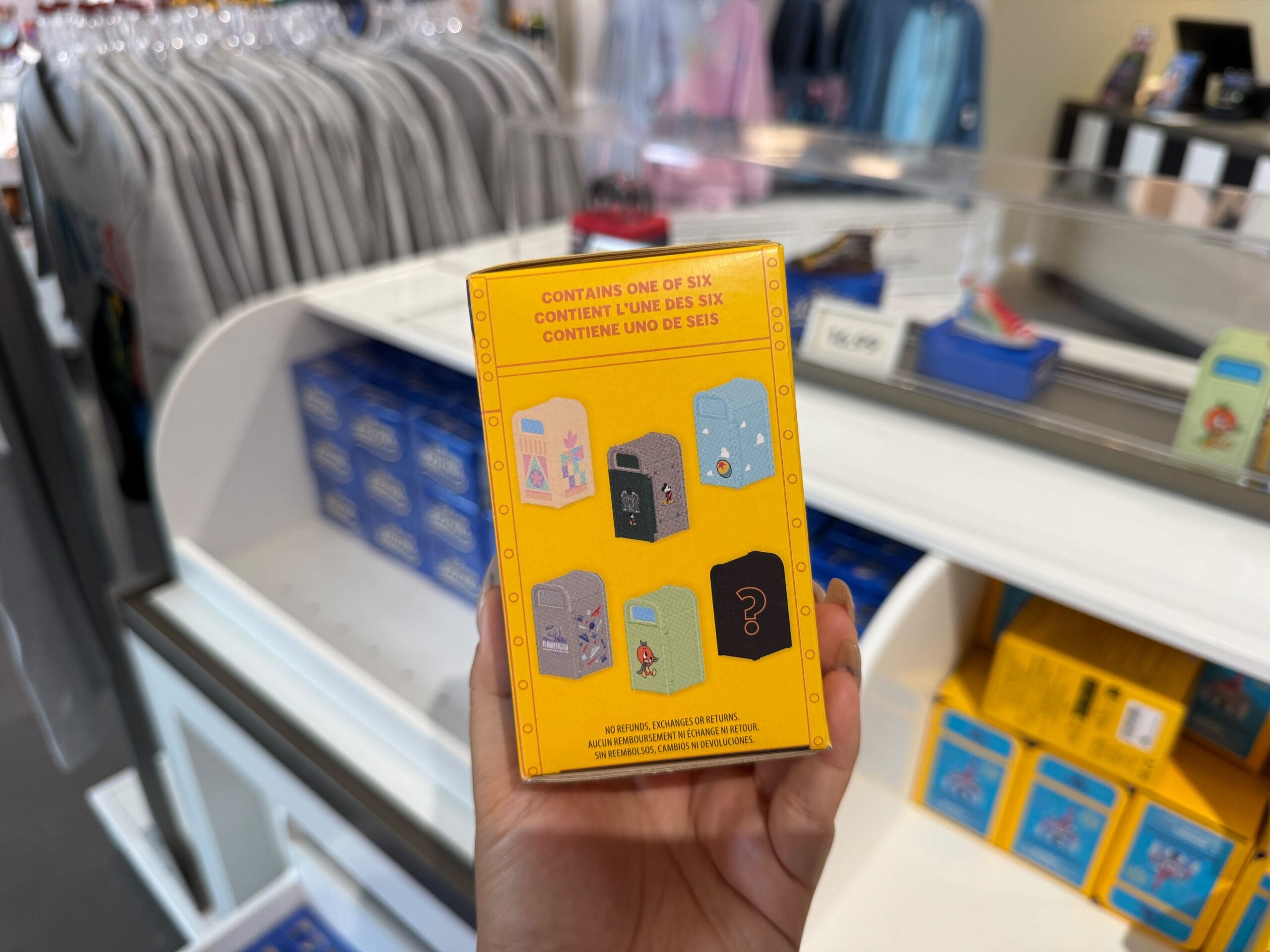 Person holding a yellow box with illustrations of six collectible pins in a retail store.