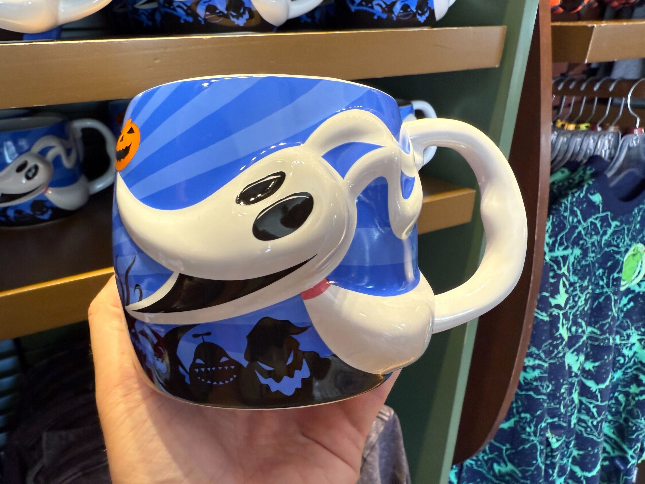 A hand holds new Nightmare Before Christmas merchandise: a mug featuring Zero the ghost dog with blue and black designs.
