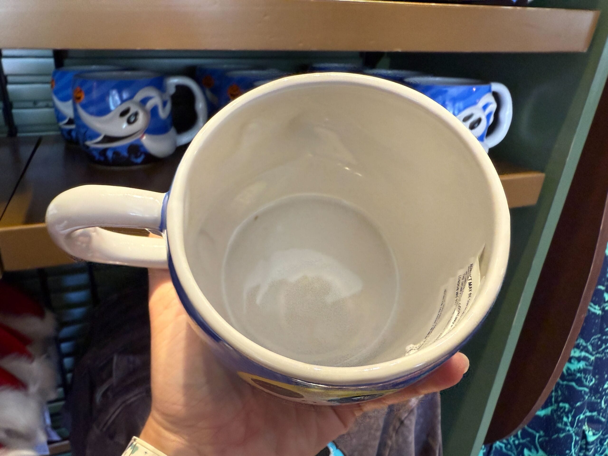 A hand holds a large empty mug above a shelf with blue Nightmare Before Christmas collectibles in the background.