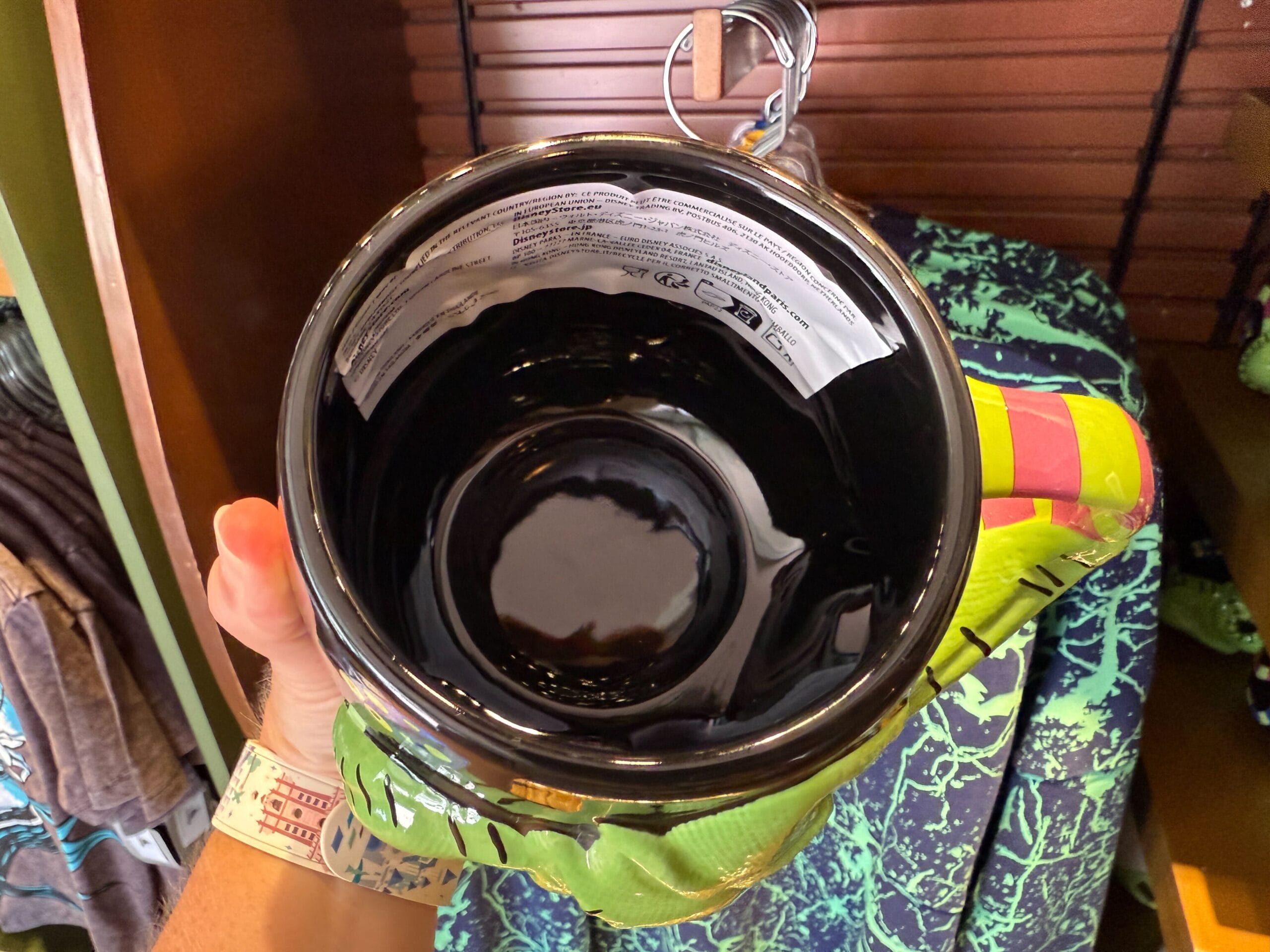 A hand holds The Nightmare Before Christmas merchandise: a large black mug with green and yellow details, label inside.