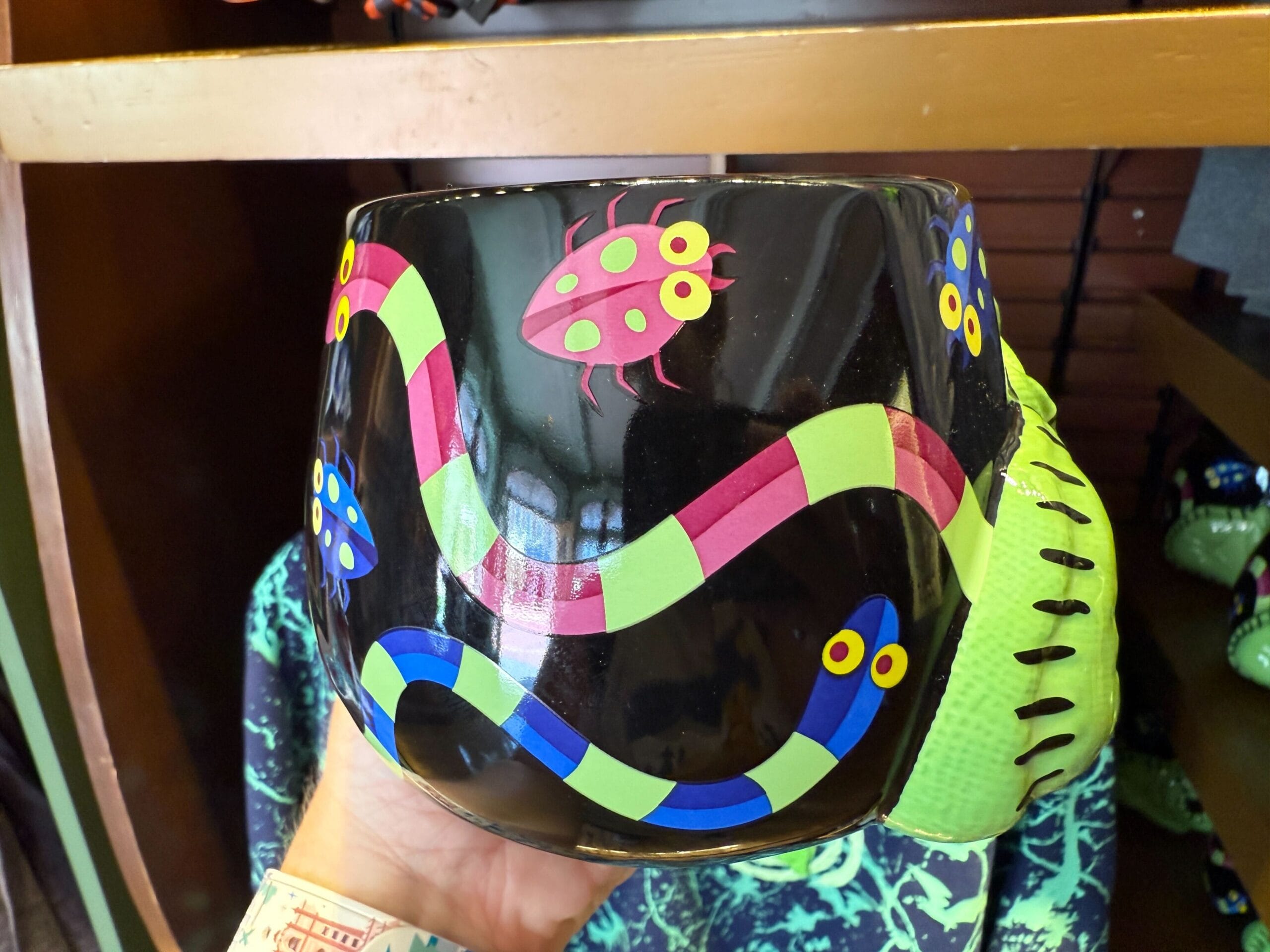 A black cup featuring colorful snakes and bugs, held in front of Nightmare Before Christmas merchandise.