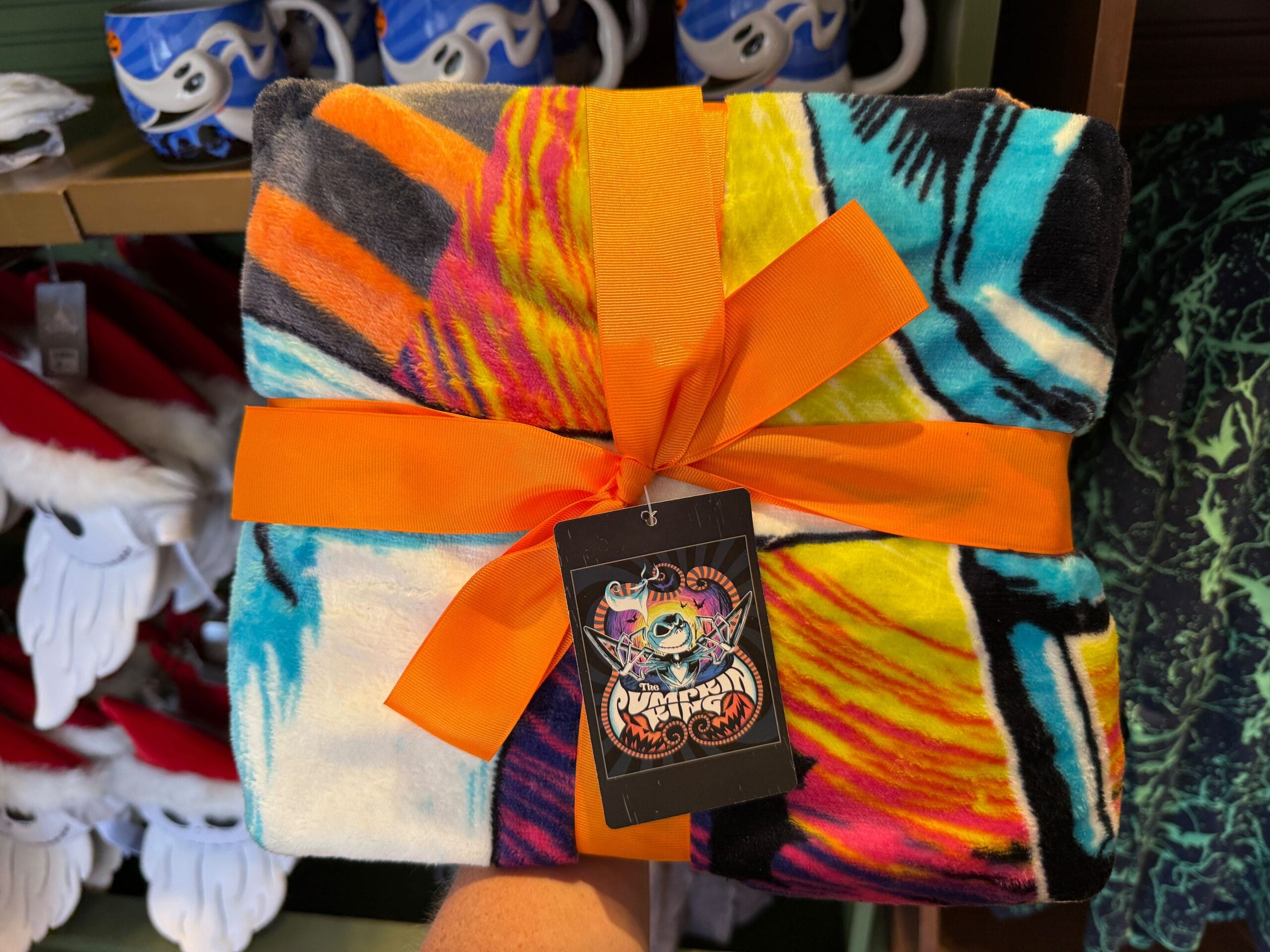 A new Nightmare Before Christmas blanket with "Pumpkin King" tag, held in front of festive holiday hats merchandise.