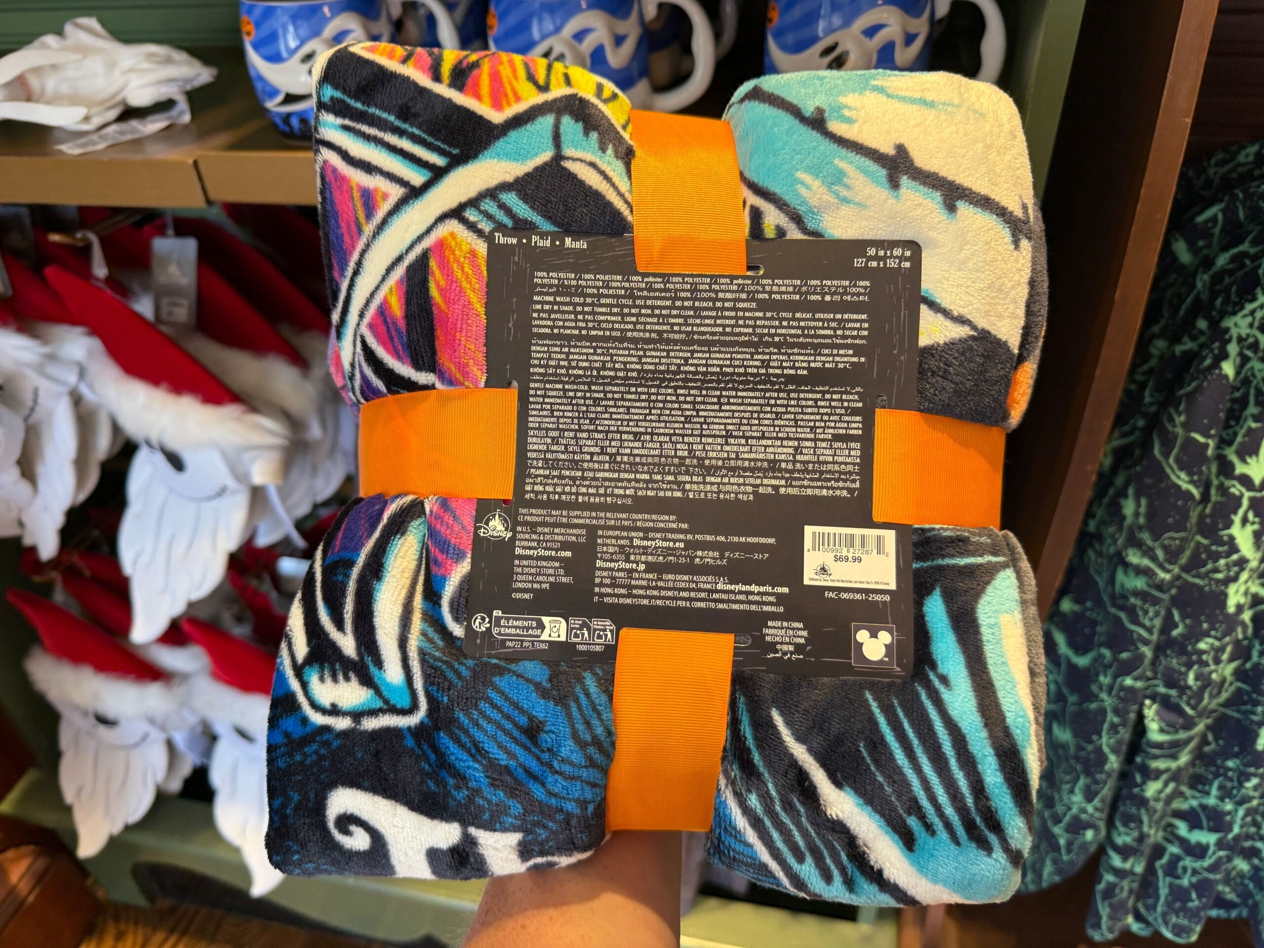 Colorful folded Nightmare Before Christmas blanket with orange straps, held in-store, label with text visible in the center.