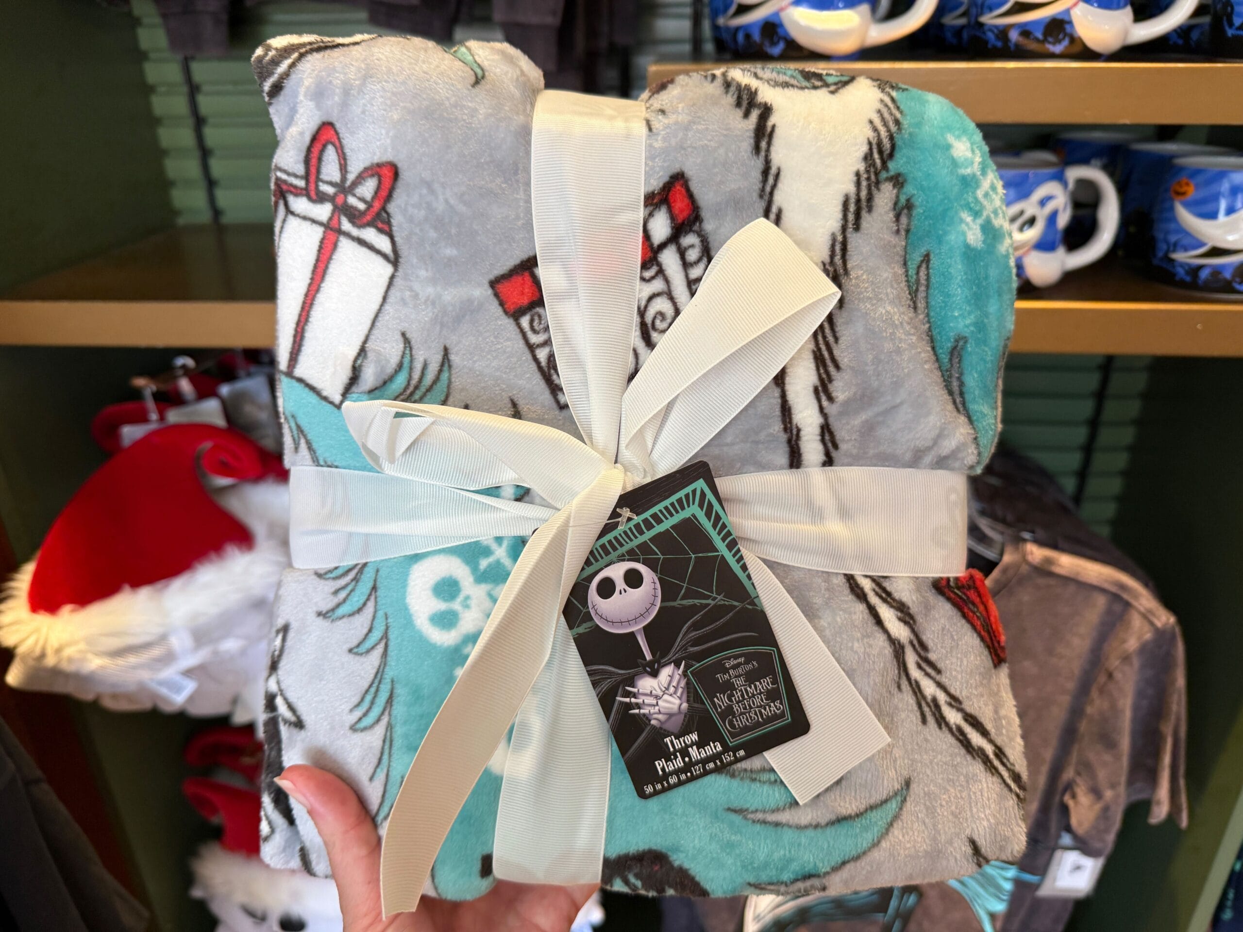 A hand holds a folded, new Nightmare Before Christmas merchandise blanket with a Jack Skellington tag and cream ribbon.