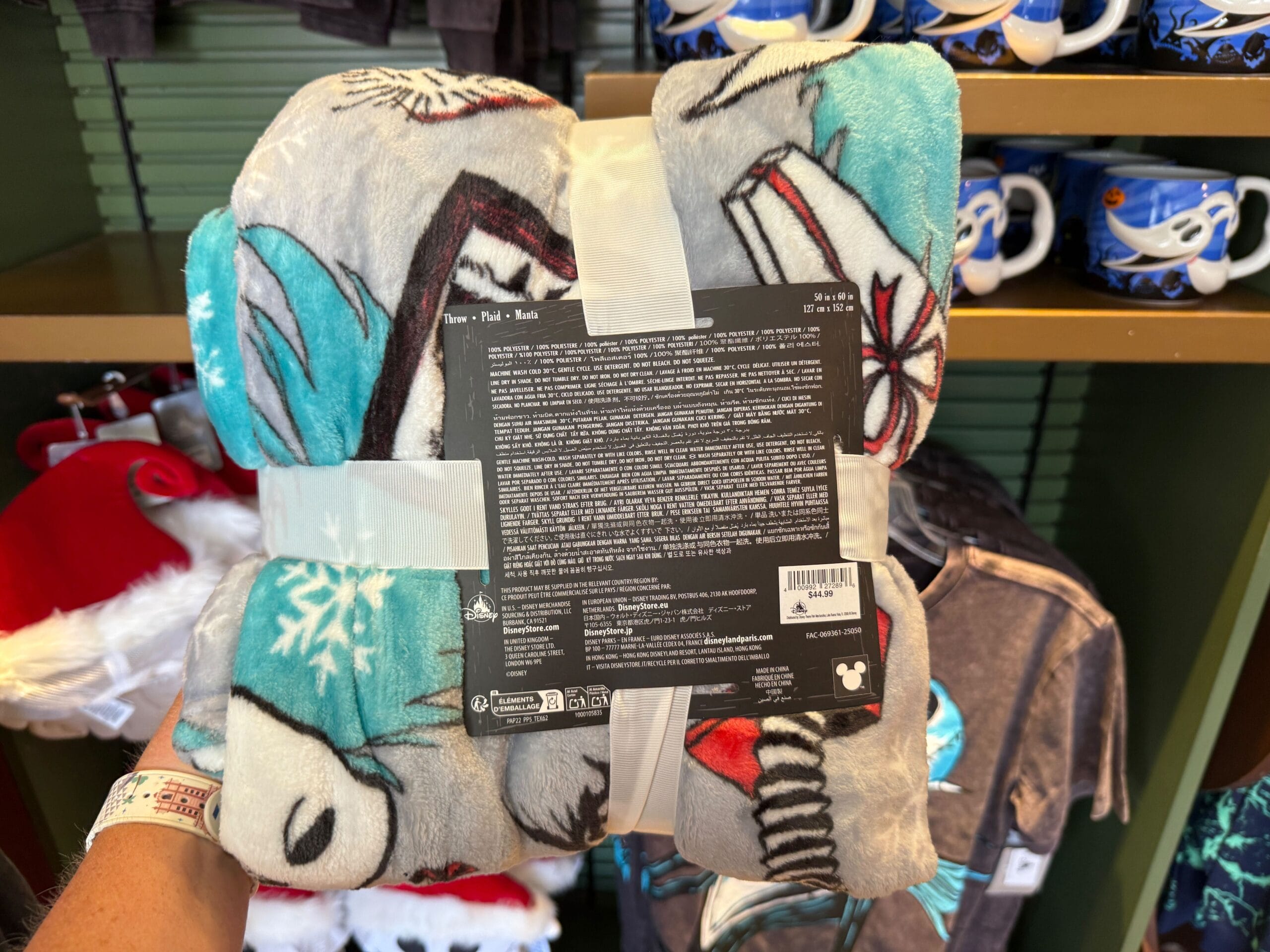 A person holds Nightmare Before Christmas merchandise—a folded Disney fleece blanket—showing its tag and design in a store.