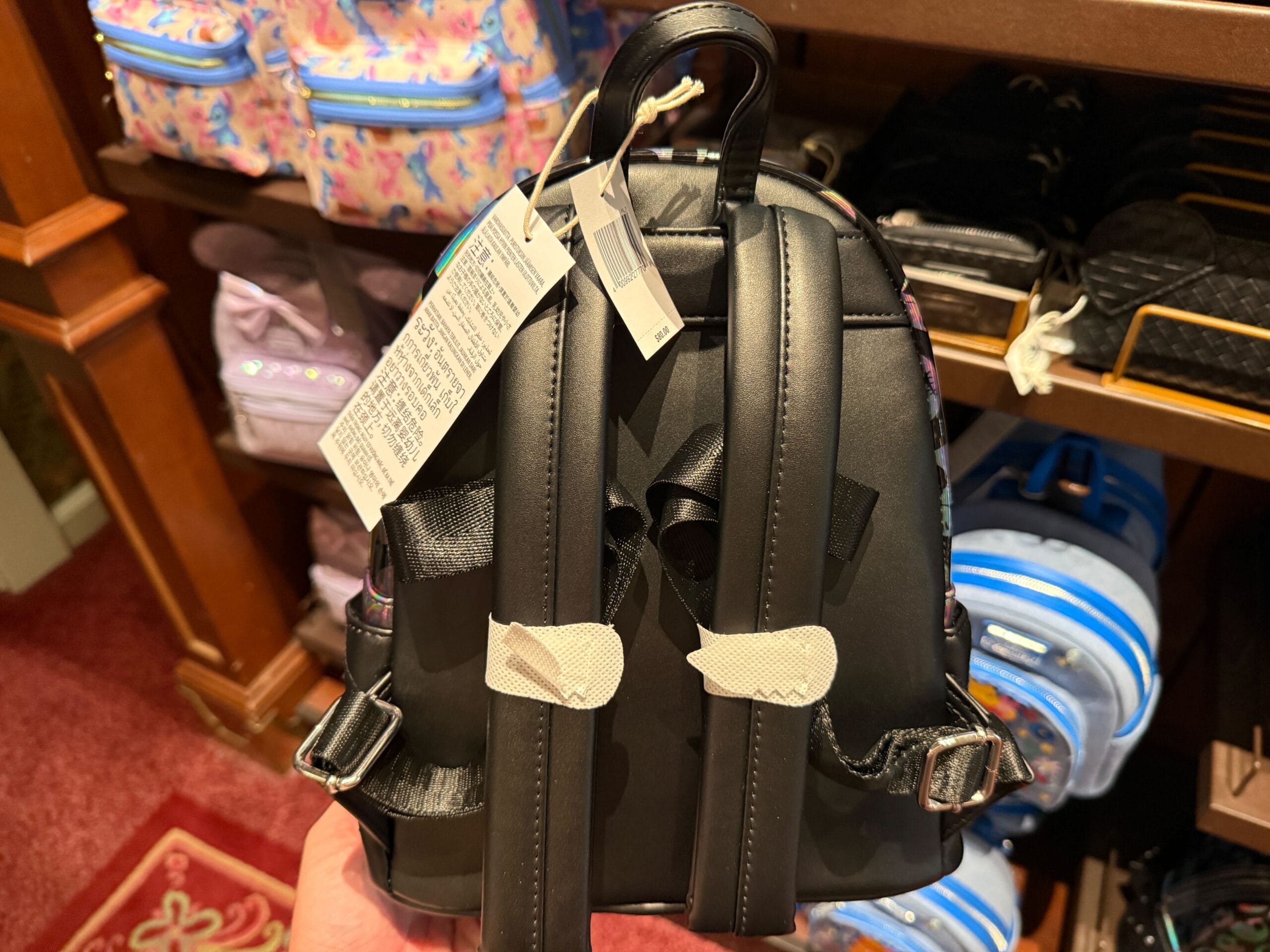 A person holds a small black backpack with tags, featuring The Nightmare Before Christmas merchandise in a store display.