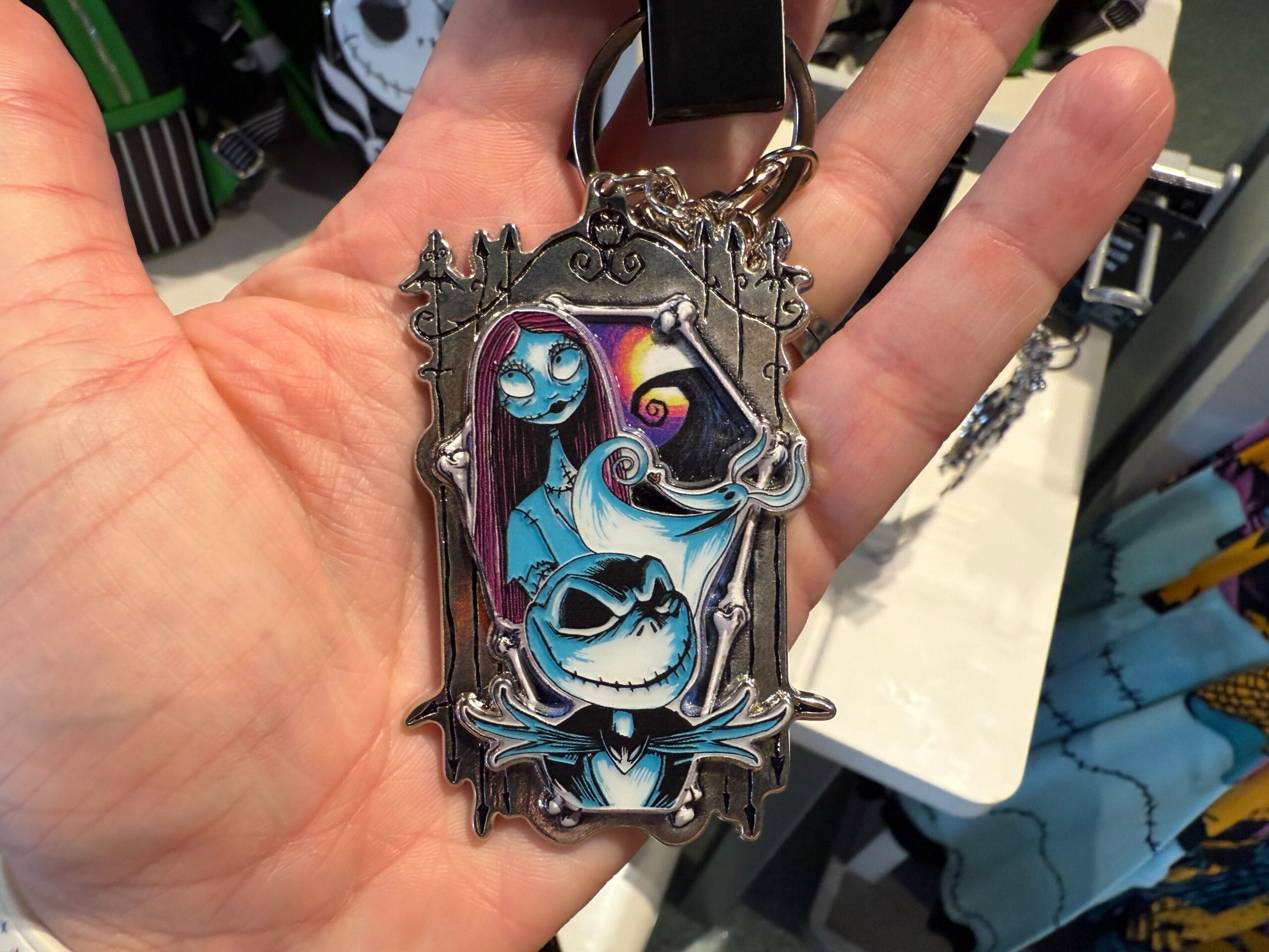 A hand holds a keychain featuring Jack Skellington and Sally—perfect Nightmare Before Christmas merchandise.