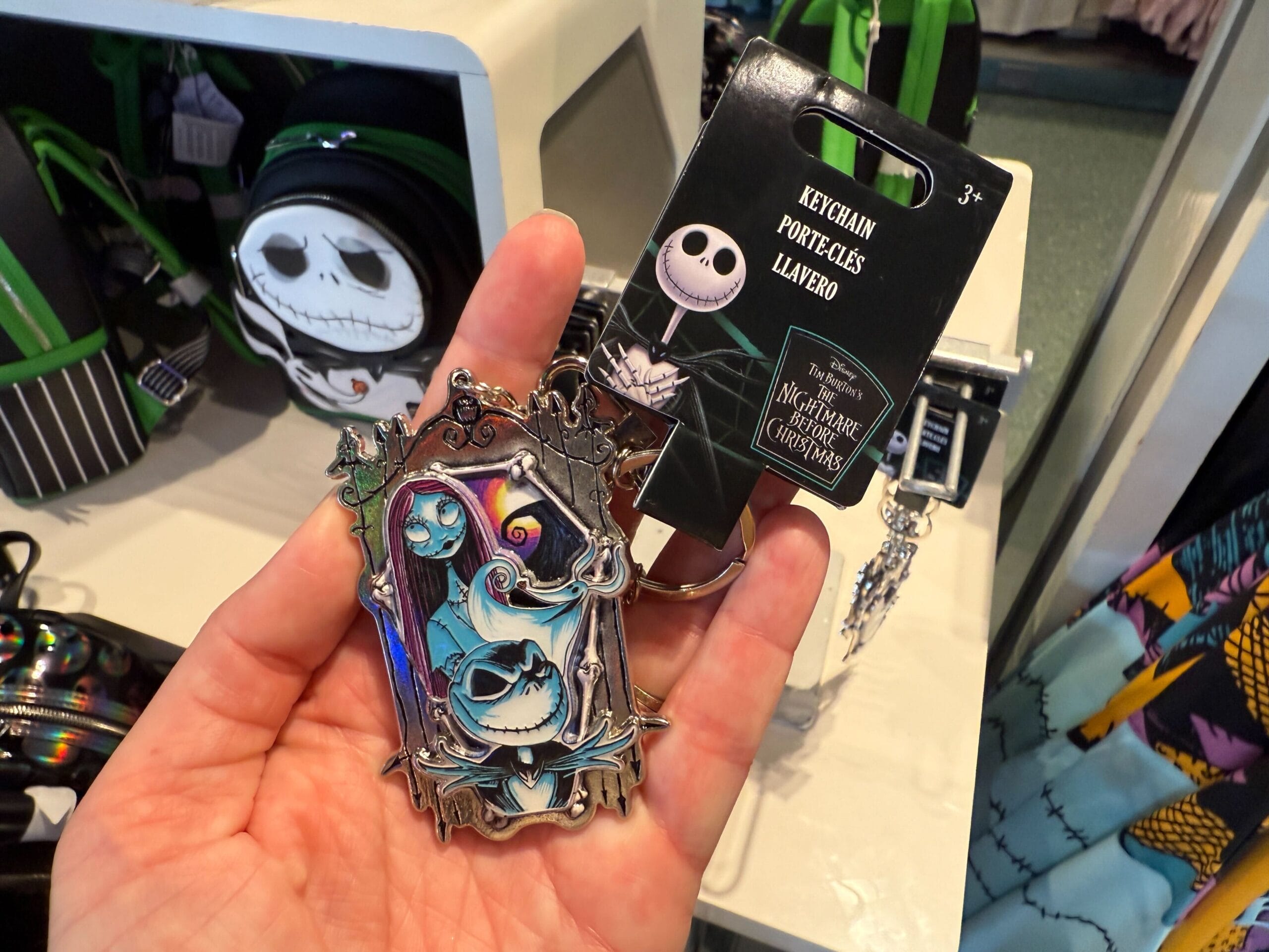Hand holding The Nightmare Before Christmas merchandise: a Jack Skellington and Sally keychain in a detailed frame.