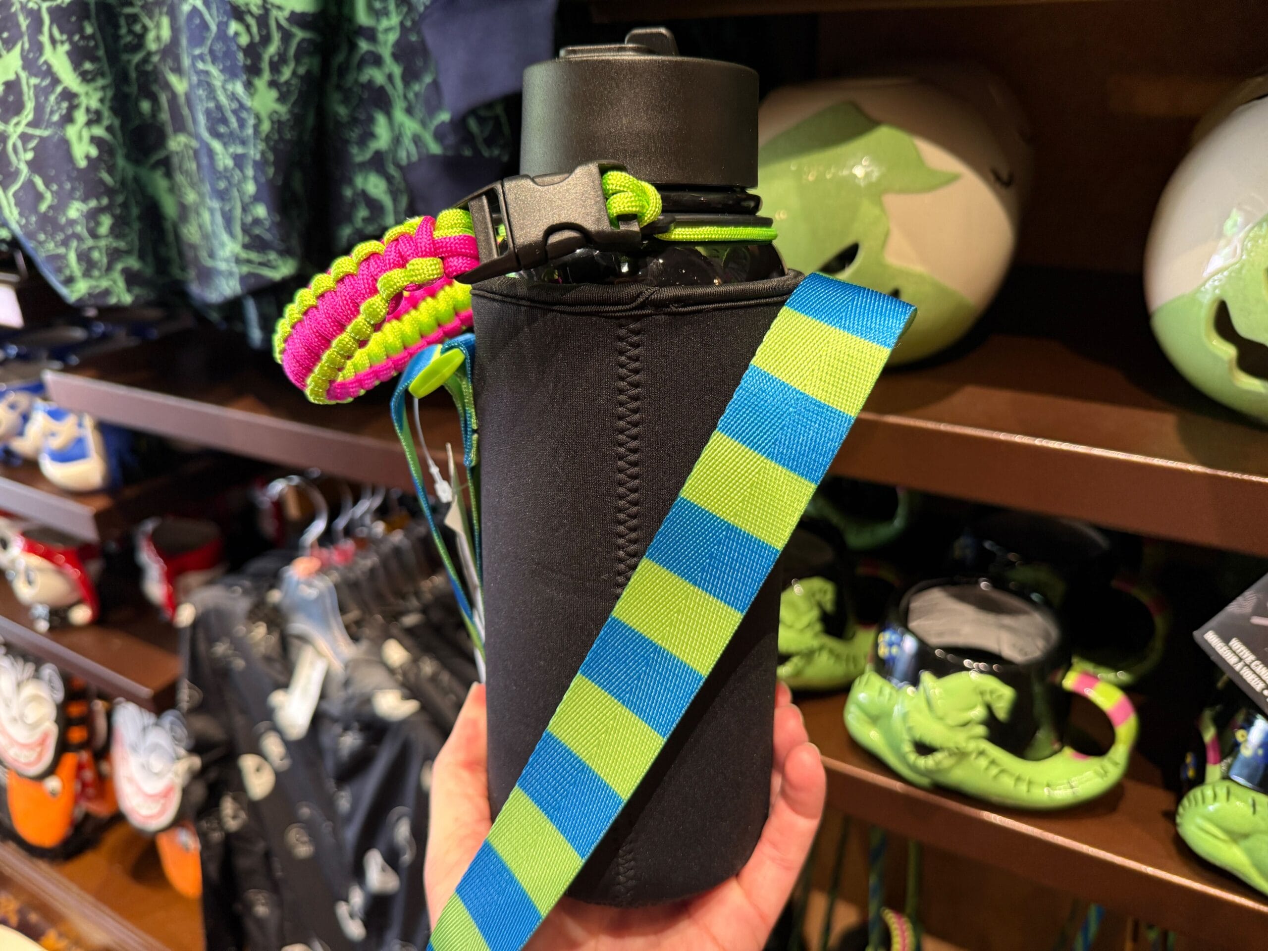 A hand holds a black water bottle with a striped strap in a store featuring Nightmare Before Christmas merchandise.
