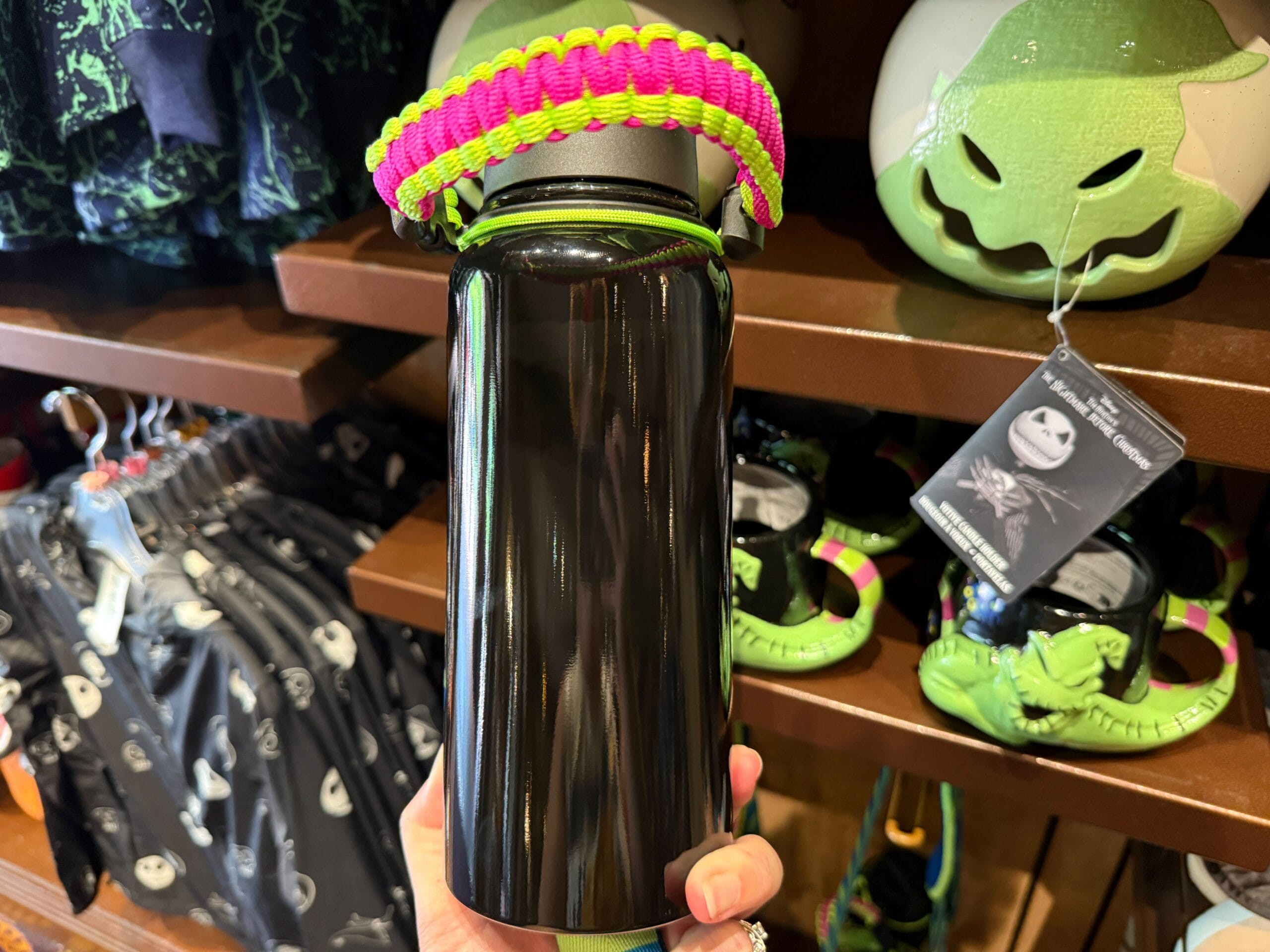 Hand holding a black water bottle with a green and pink handle amid new Nightmare Before Christmas merchandise in store.
