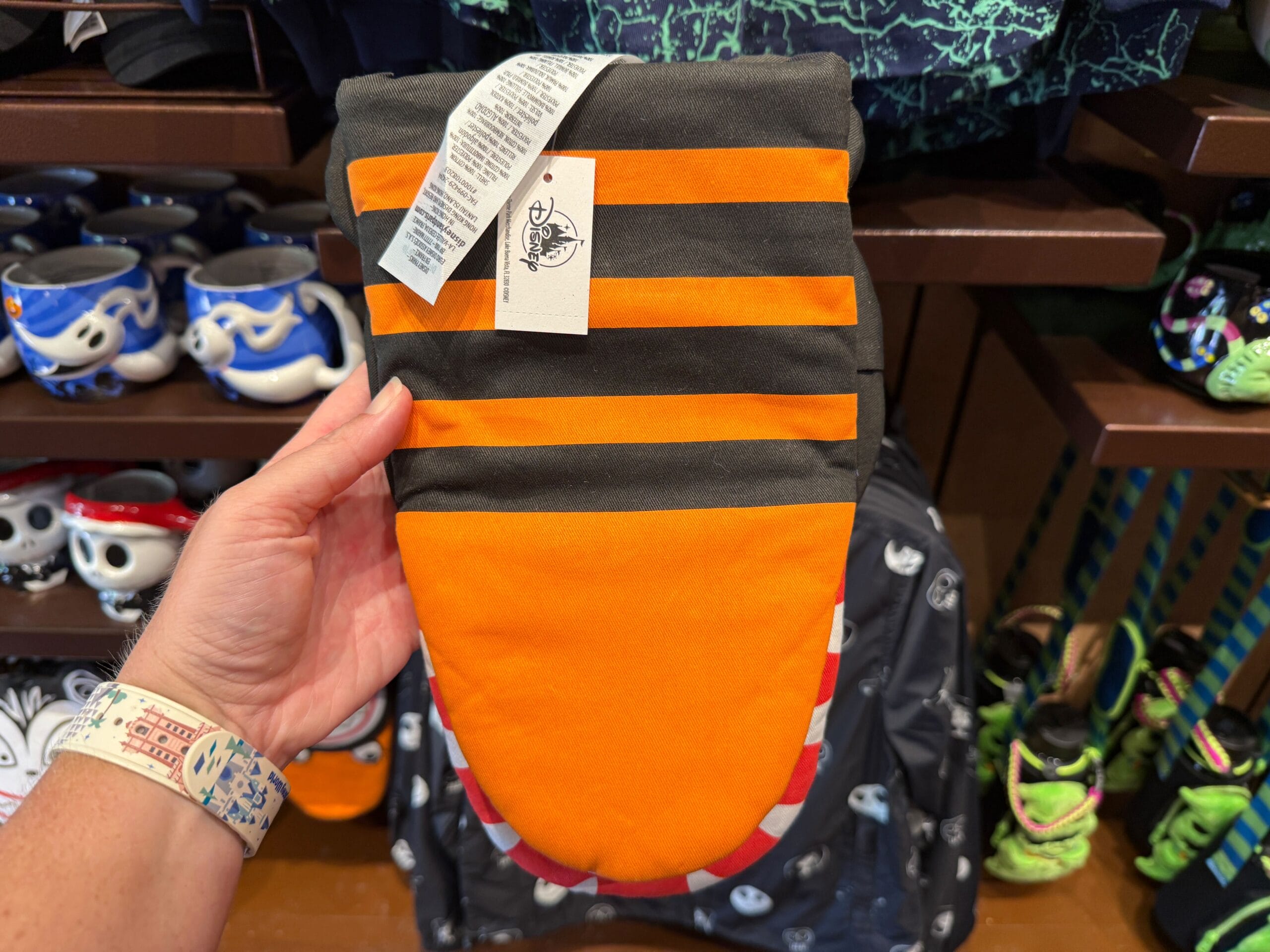 A hand holds The Nightmare Before Christmas merchandise; spooky mugs and bags are displayed in the background.