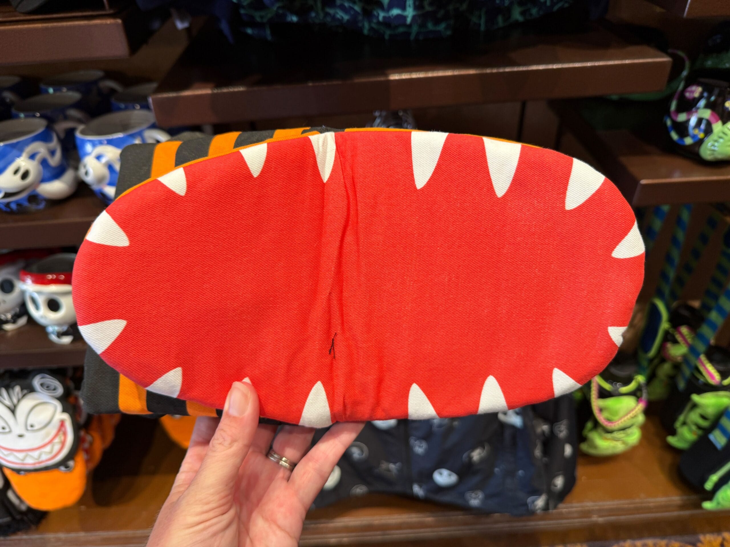 A hand holds a red mask with white triangular teeth, resembling The Nightmare Before Christmas merchandise.