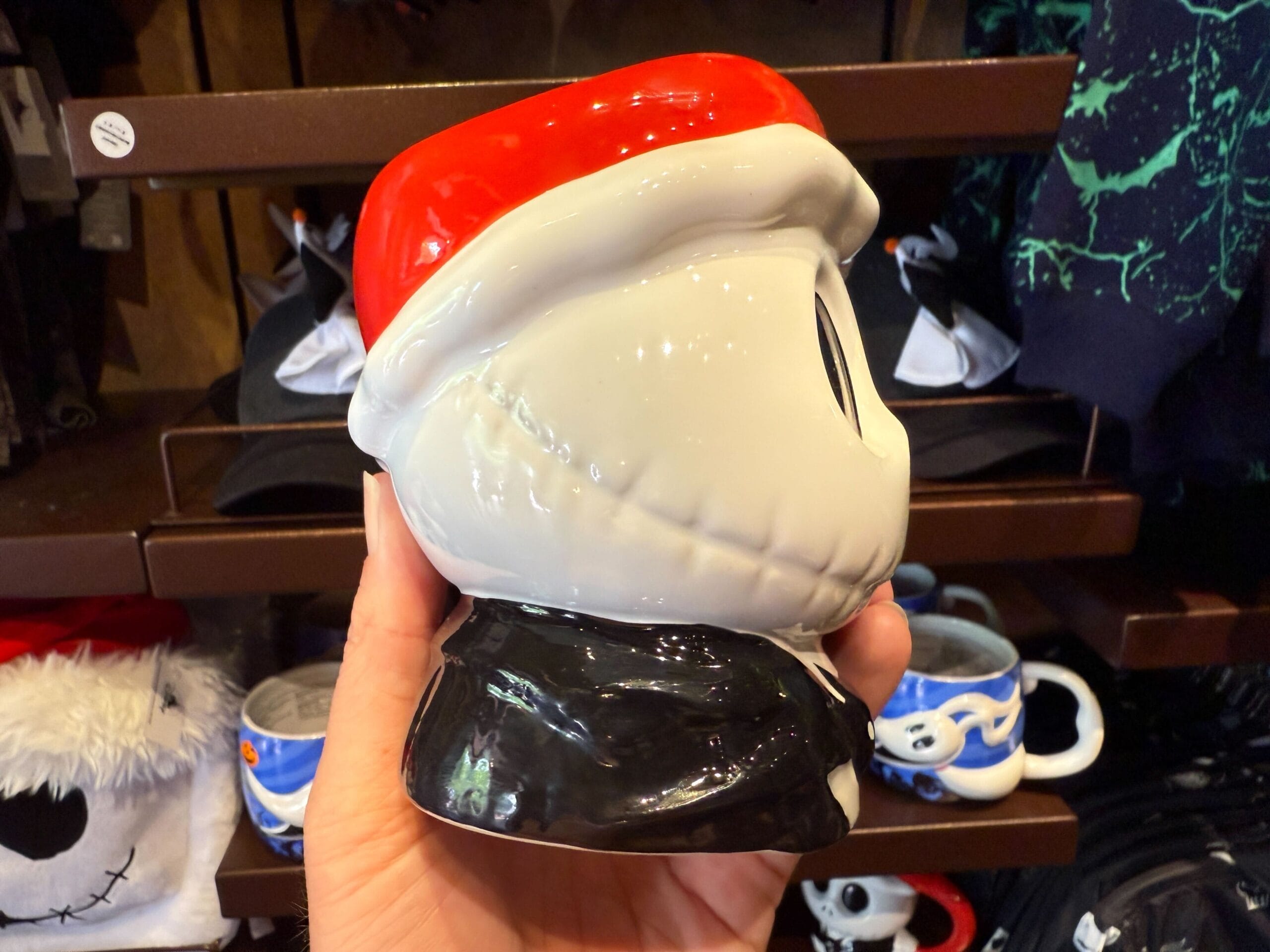 A hand holds Nightmare Before Christmas merchandise—a ceramic mug shaped like Jack Skellington in a Santa hat.