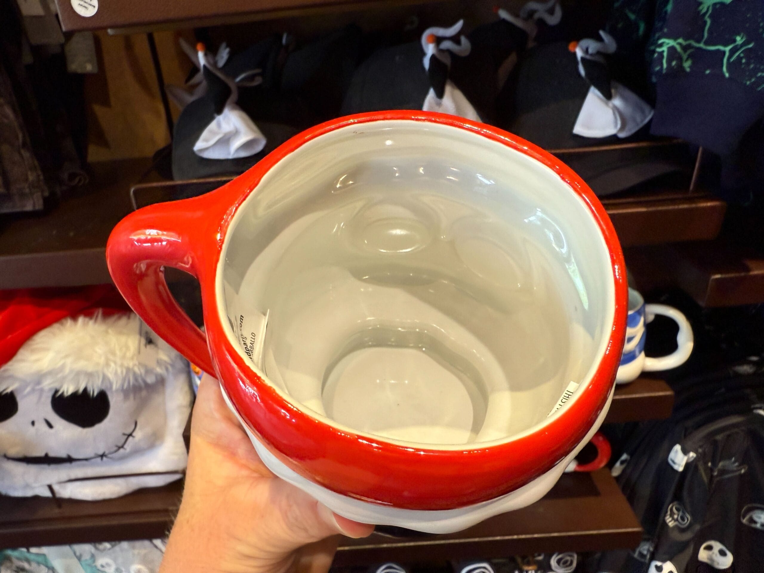 A hand holds a large red and white mug shaped like Jack Skellington’s head—iconic The Nightmare Before Christmas merchandise.