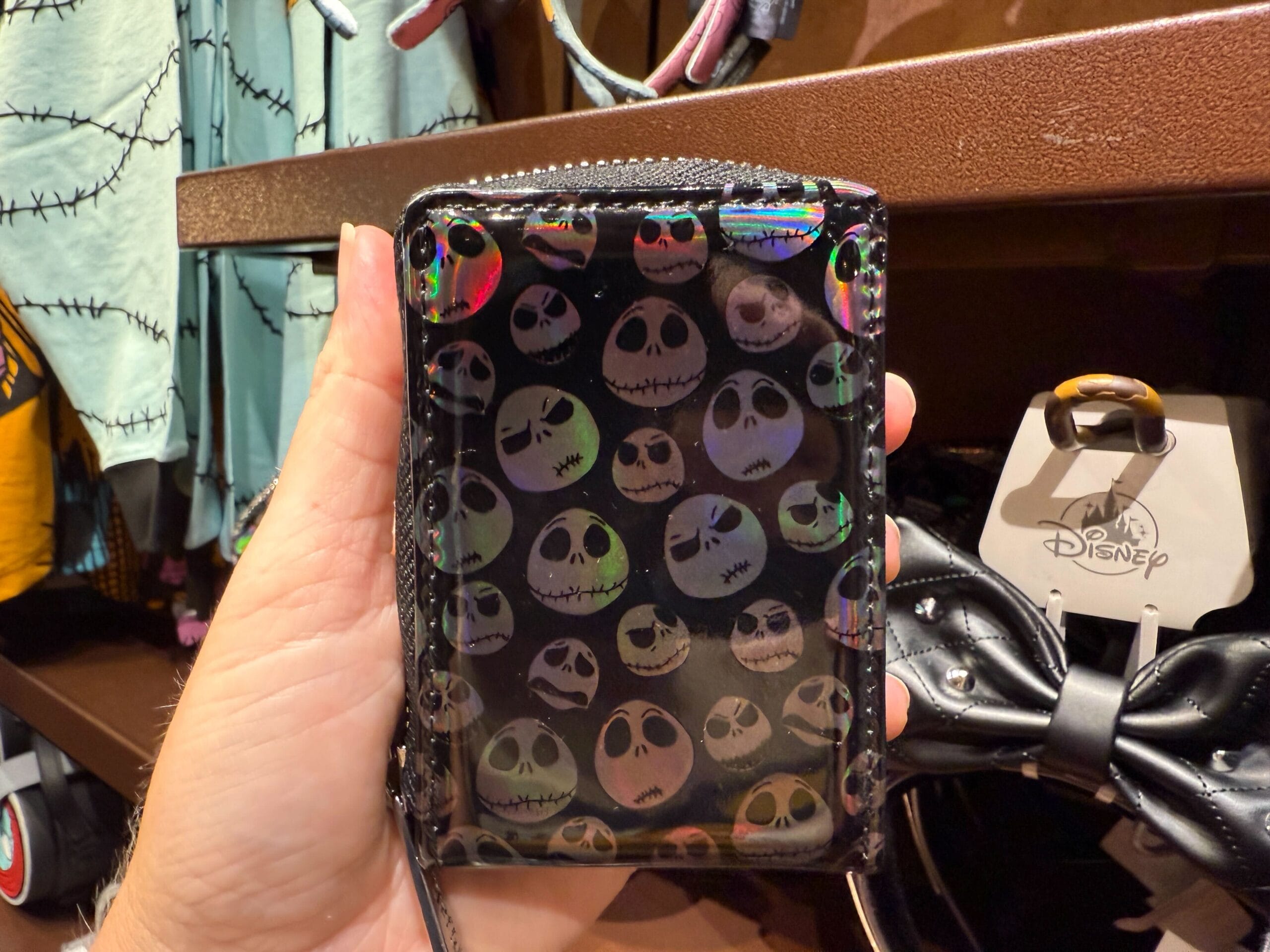 A hand holds The Nightmare Before Christmas merchandise: a wallet patterned with Jack Skellington faces.