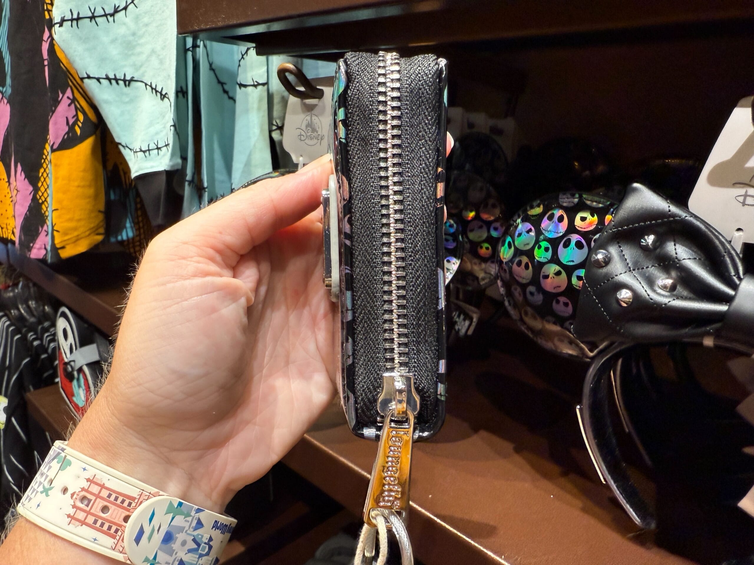 A hand holds a small black zippered wallet with The Nightmare Before Christmas accessories in the background.