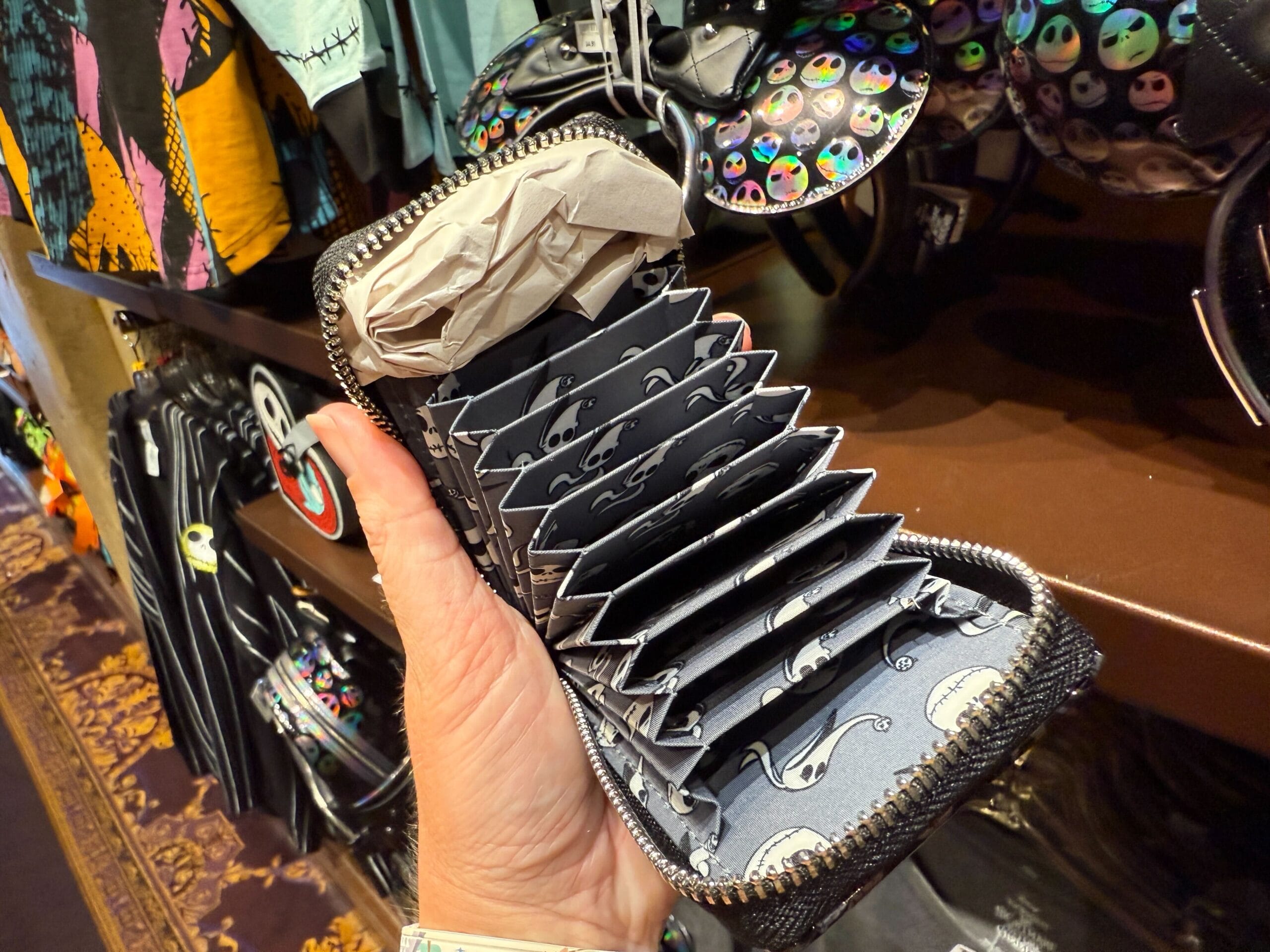 A hand holds an open Nightmare Before Christmas merchandise wallet, revealing card slots with Jack Skellington prints.