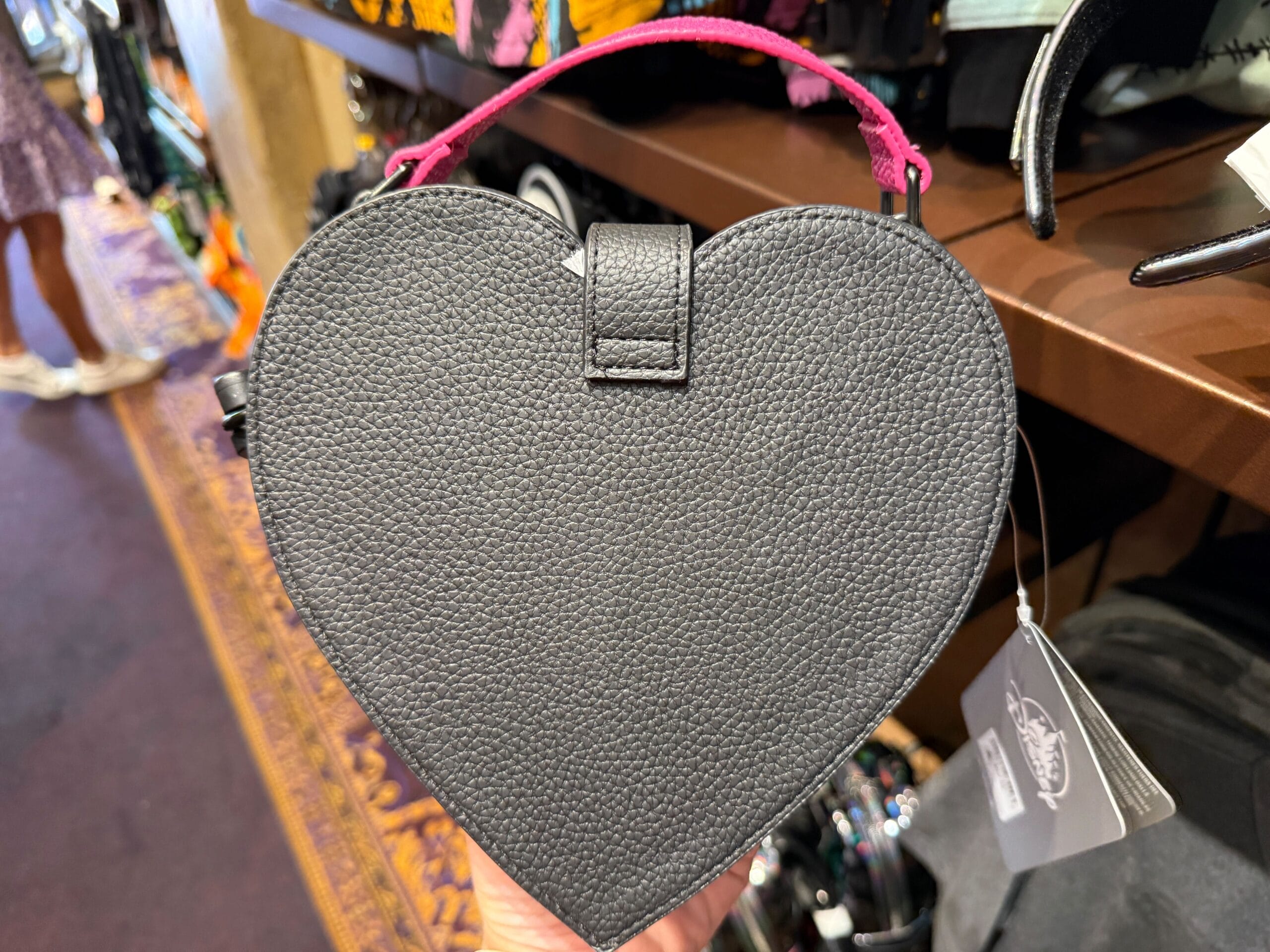 A black, heart-shaped Nightmare Before Christmas handbag with a pink handle is displayed in a store.