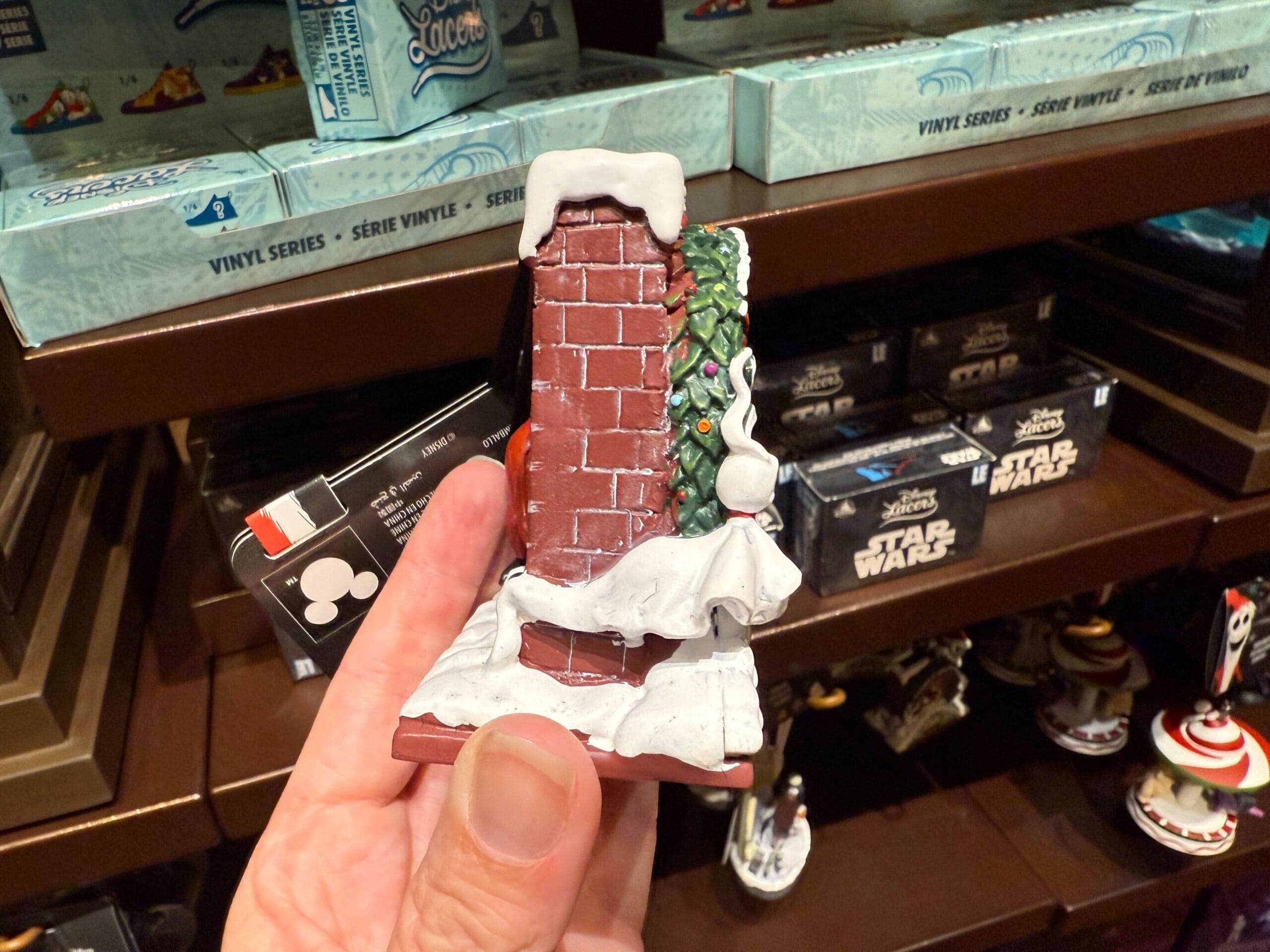 Hand holding holiday merchandise: a snowy brick chimney with Christmas tree, inspired by The Nightmare Before Christmas.