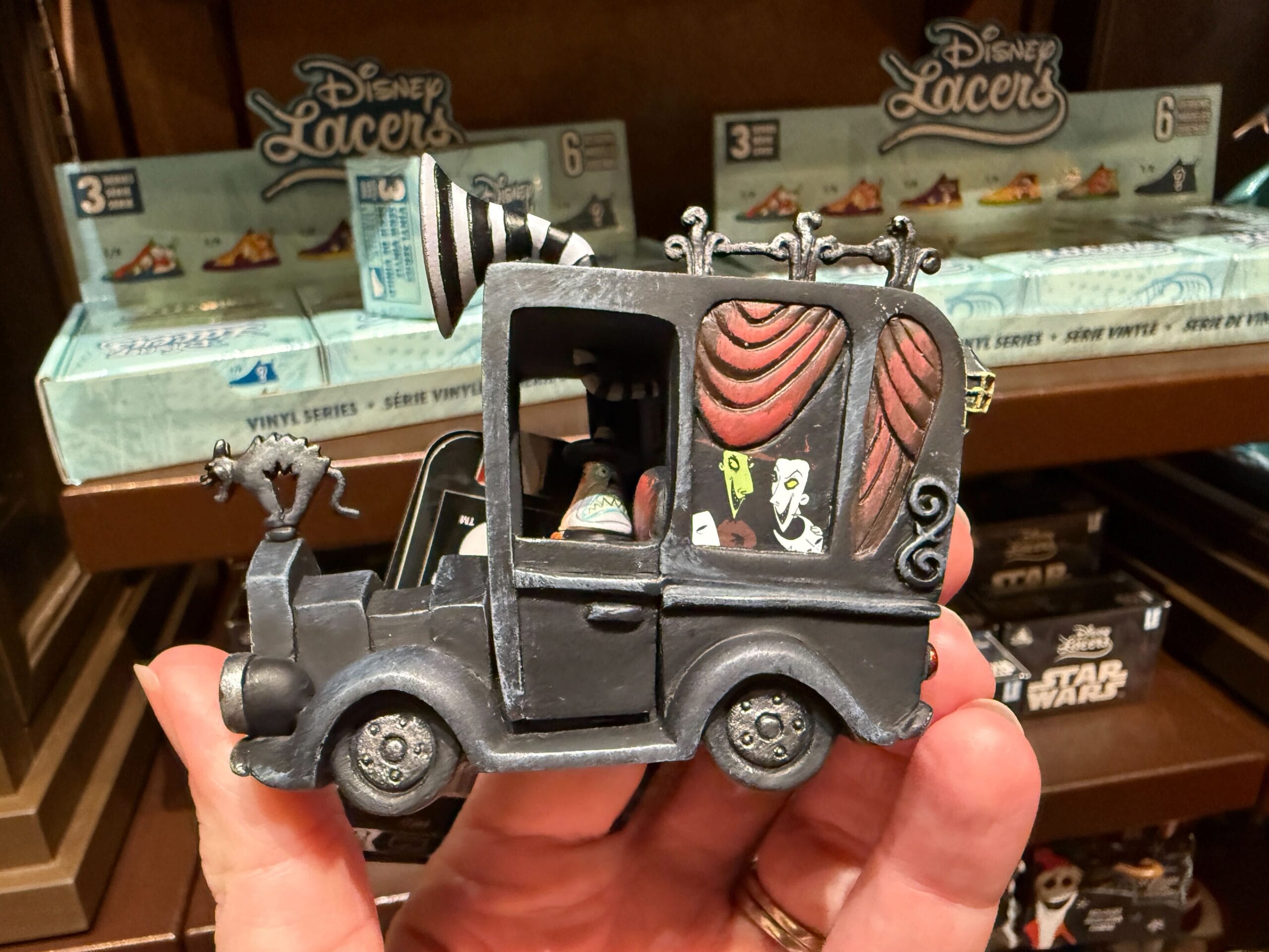 Hand holding Nightmare Before Christmas merchandise: a toy hearse with spooky details and beloved movie characters.