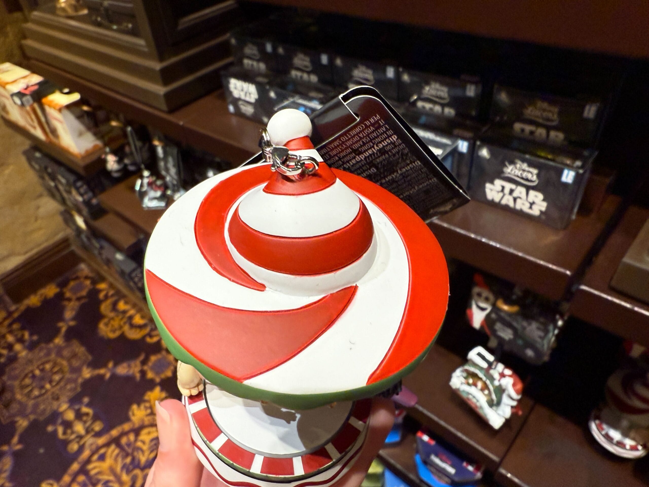 A hand holds a red and white striped ornament in a store, with The Nightmare Before Christmas merchandise in the background.