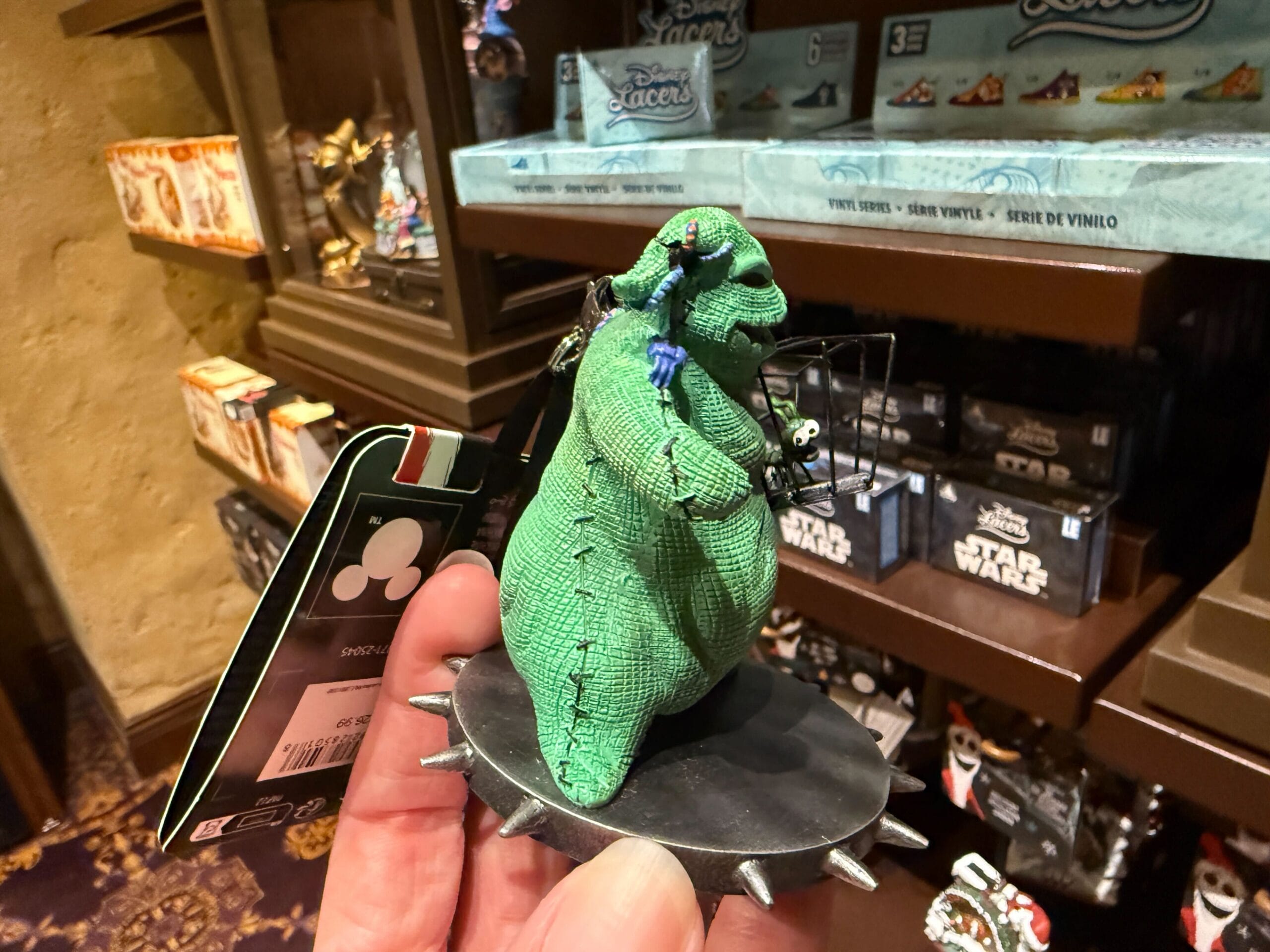 A hand holds "The Nightmare Before Christmas" merchandise—a green Oogie Boogie figurine—in a store.