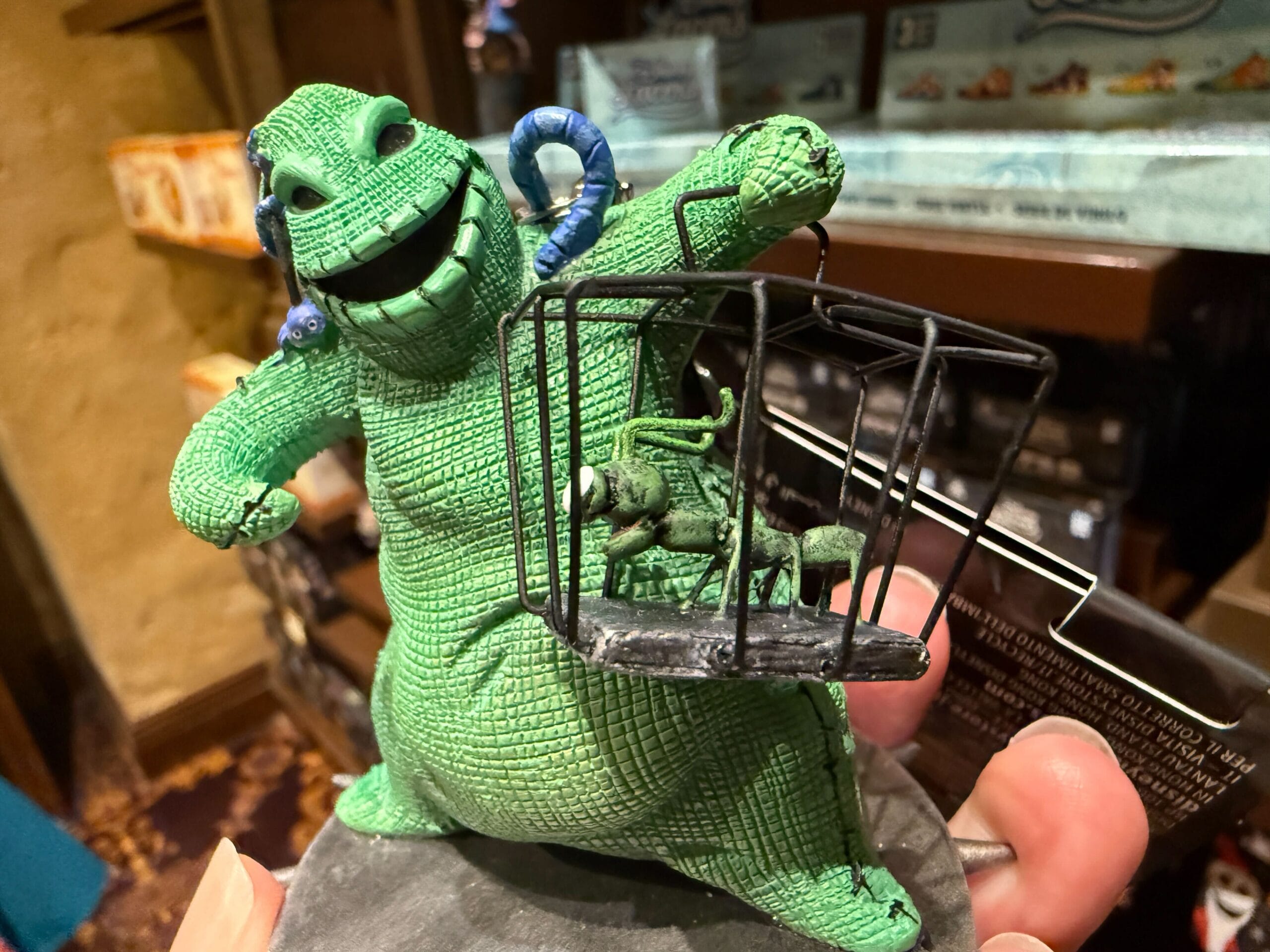 A green, grinning Oogie Boogie figurine from The Nightmare Before Christmas holds a small black cage with a bug inside.