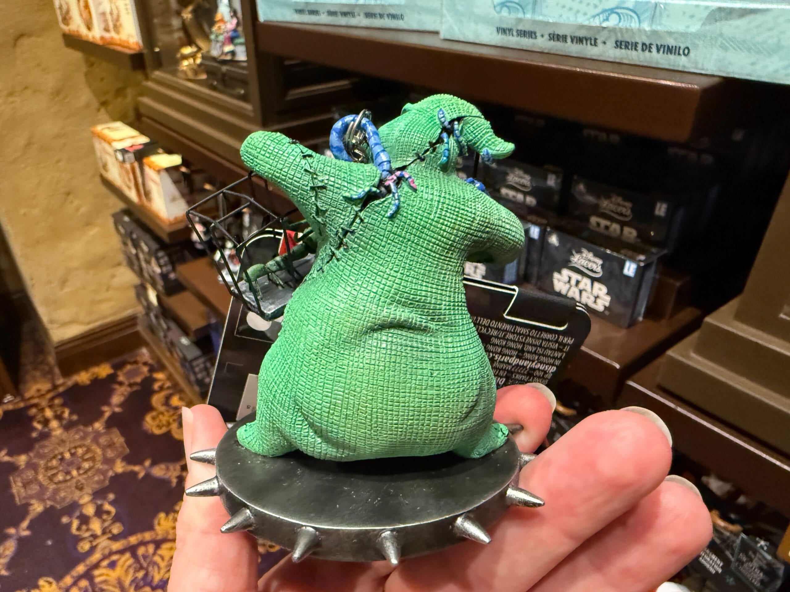 A hand holds The Nightmare Before Christmas merchandise—a green Oogie Boogie figurine—in a store.