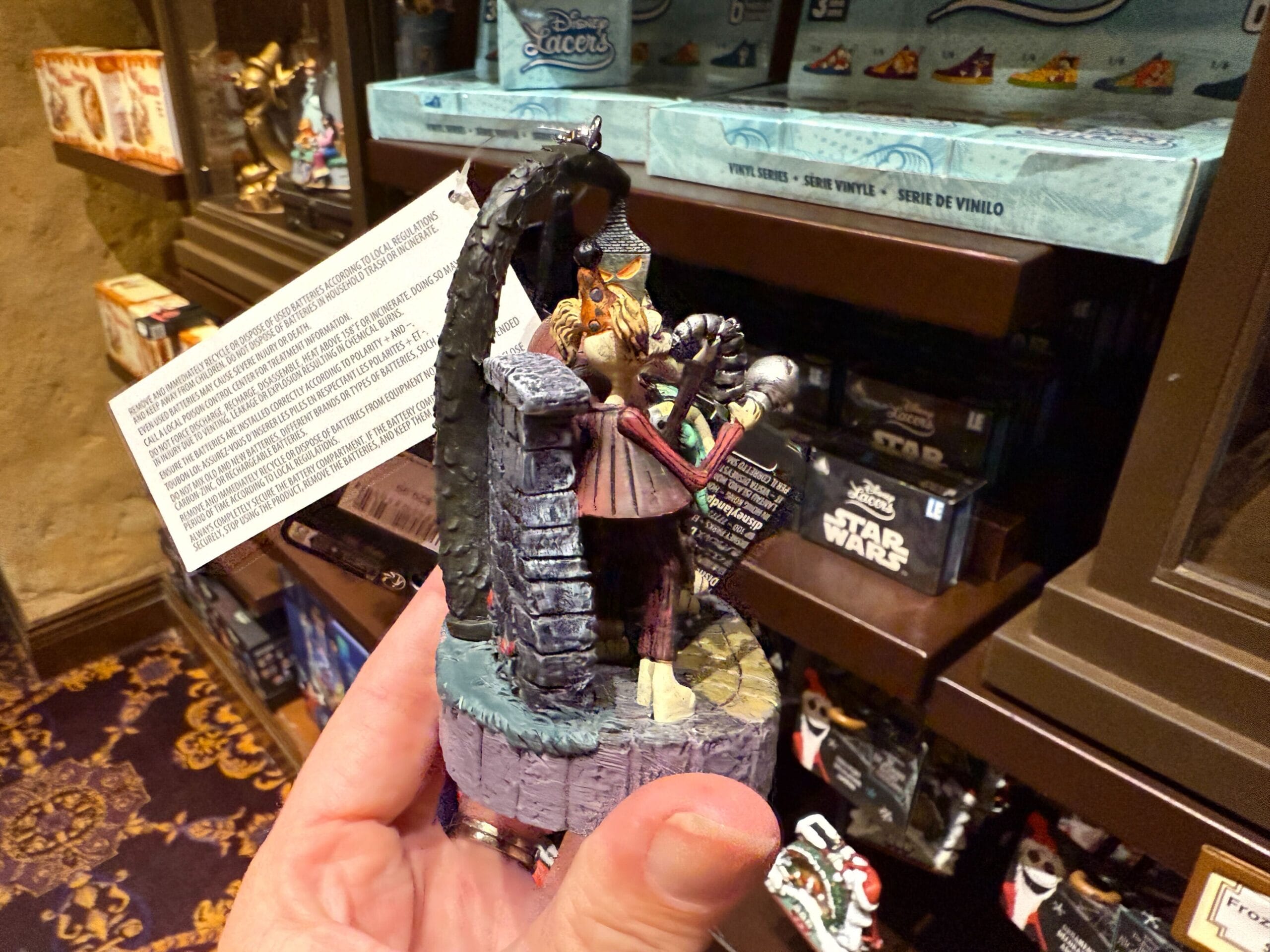 A hand holds a Sally figurine from Nightmare Before Christmas merchandise in a store with Disney and Star Wars items on display.
