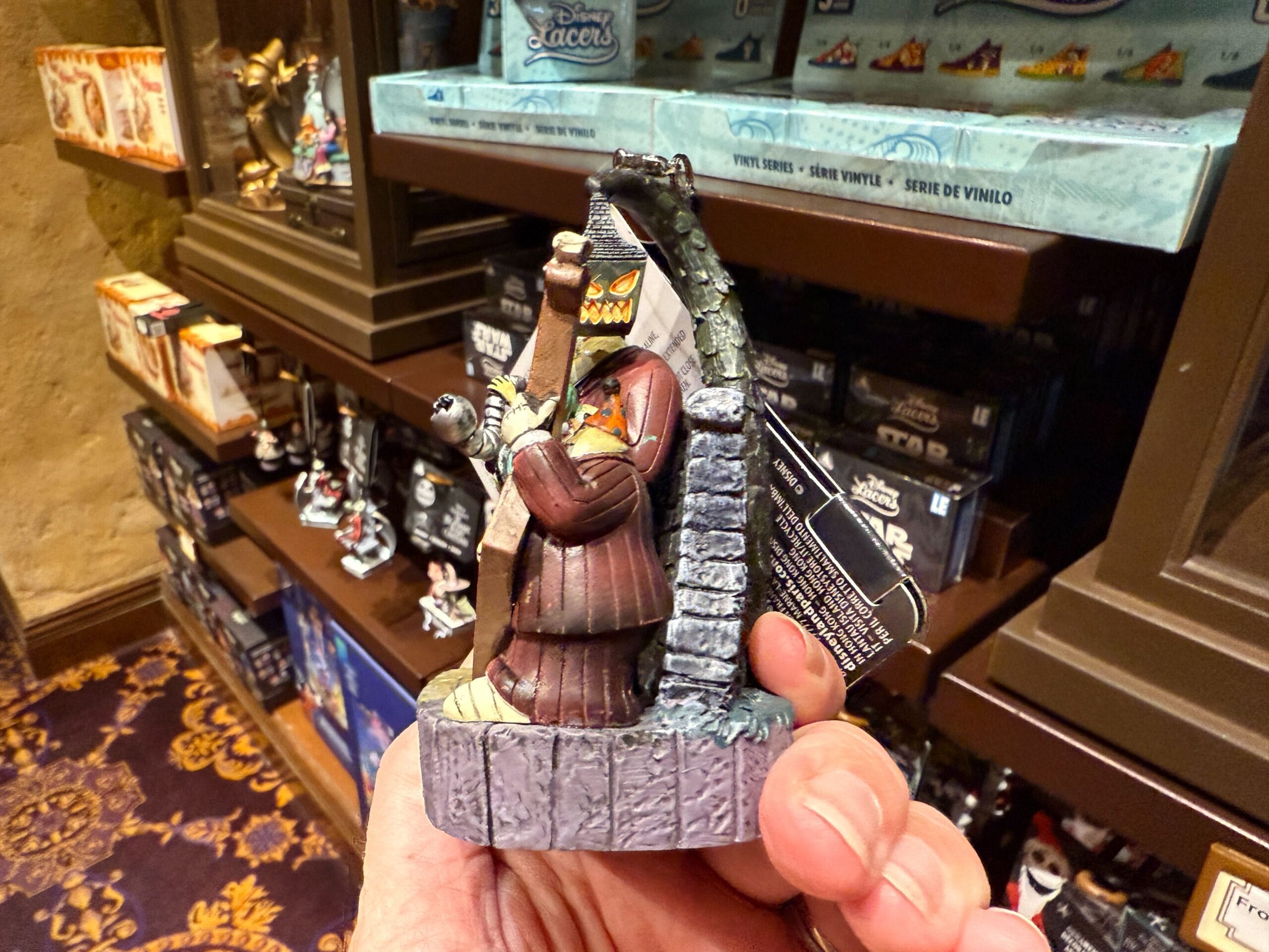 A hand holds The Nightmare Before Christmas merchandise: a judge Oogie Boogie figurine, surrounded by collectible shelves.