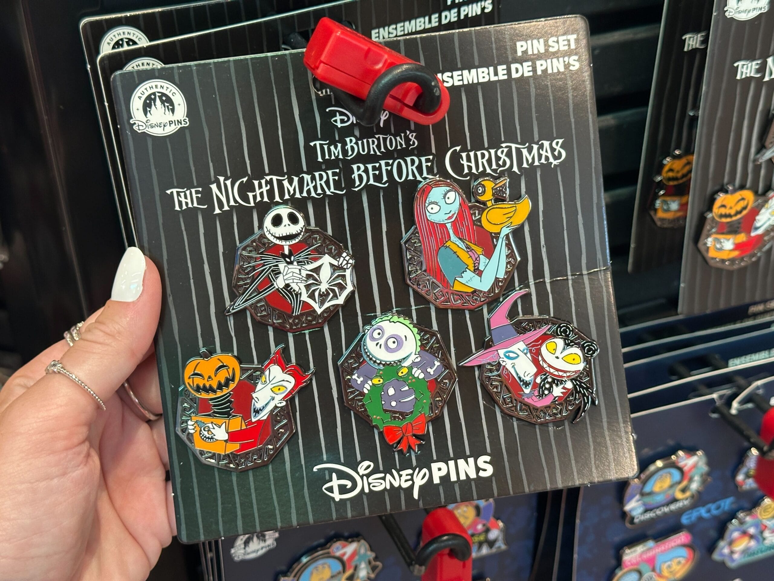 A hand holds five “Nightmare Before Christmas” merchandise pins featuring the film’s main characters.