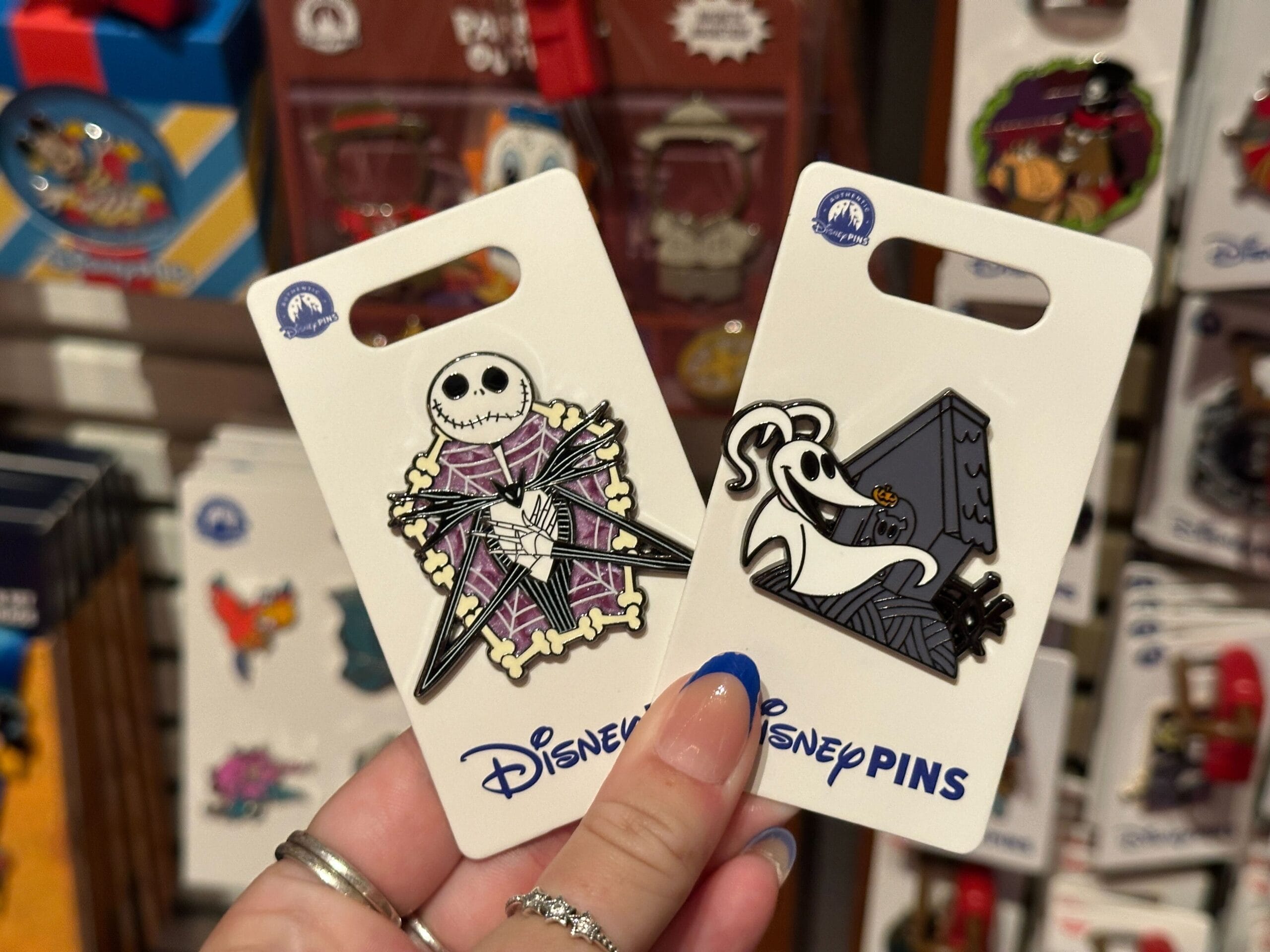 Two Disney pins featuring Jack Skellington and Zero from "The Nightmare Before Christmas" held in someone's hand.