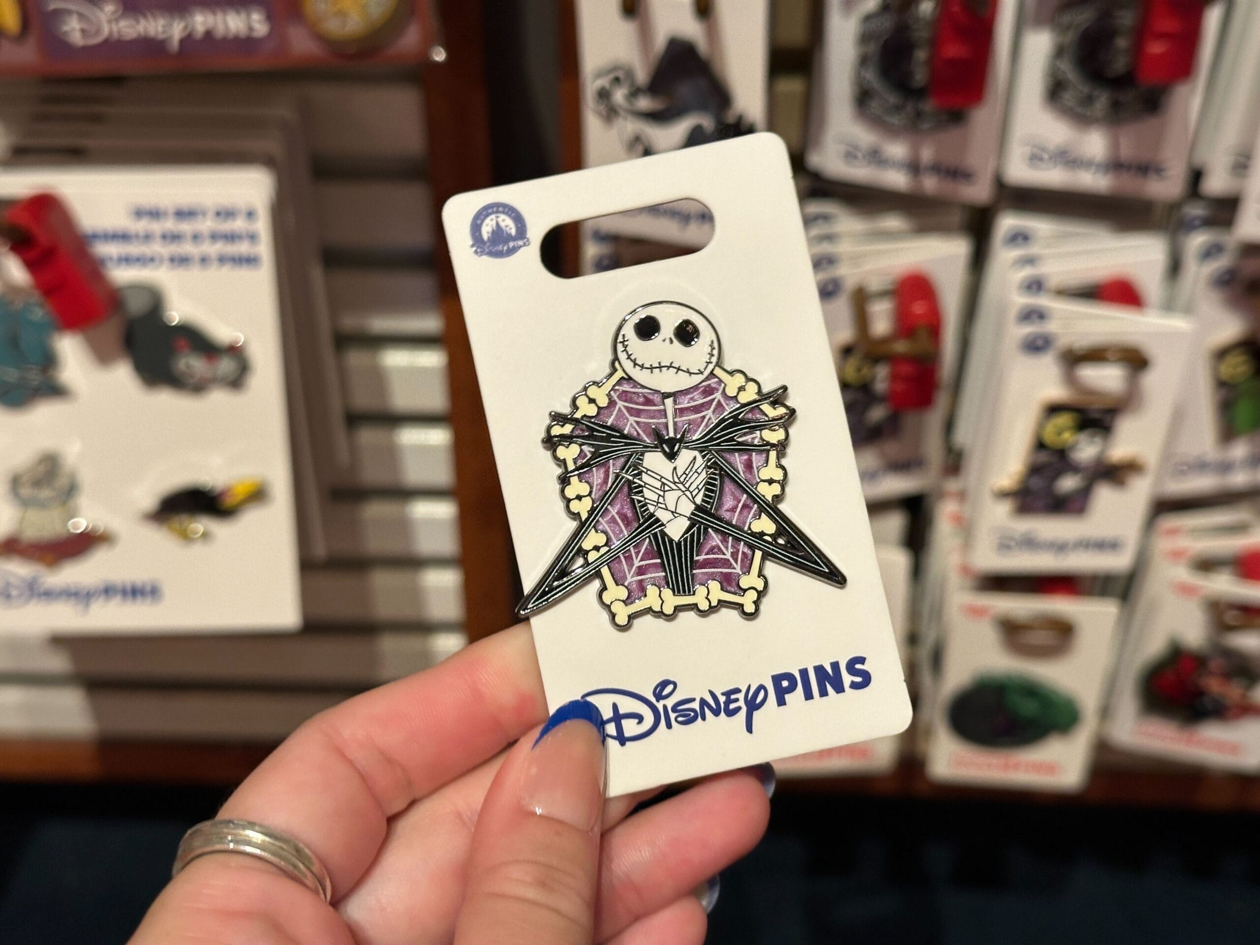 A hand holds a Disney pin featuring Jack Skellington in front of other Nightmare Before Christmas pins.