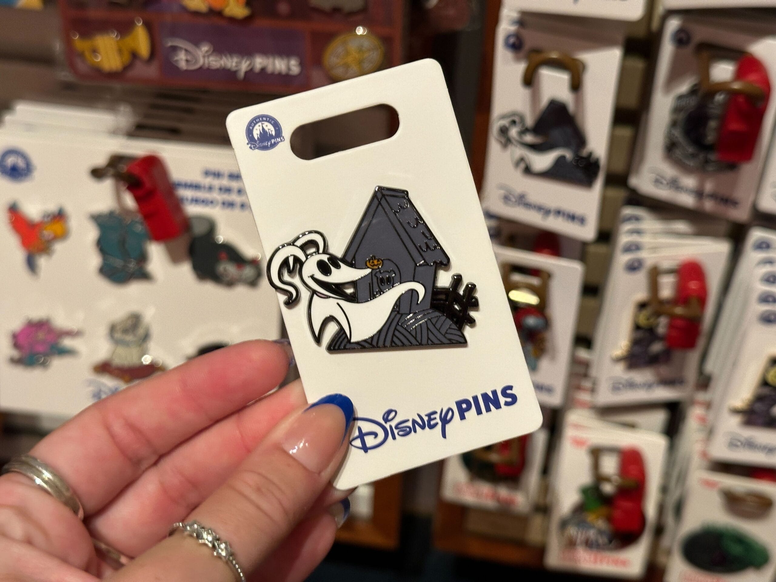 A hand holds a Disney pin featuring Zero the ghost dog in front of his doghouse from The Nightmare Before Christmas.