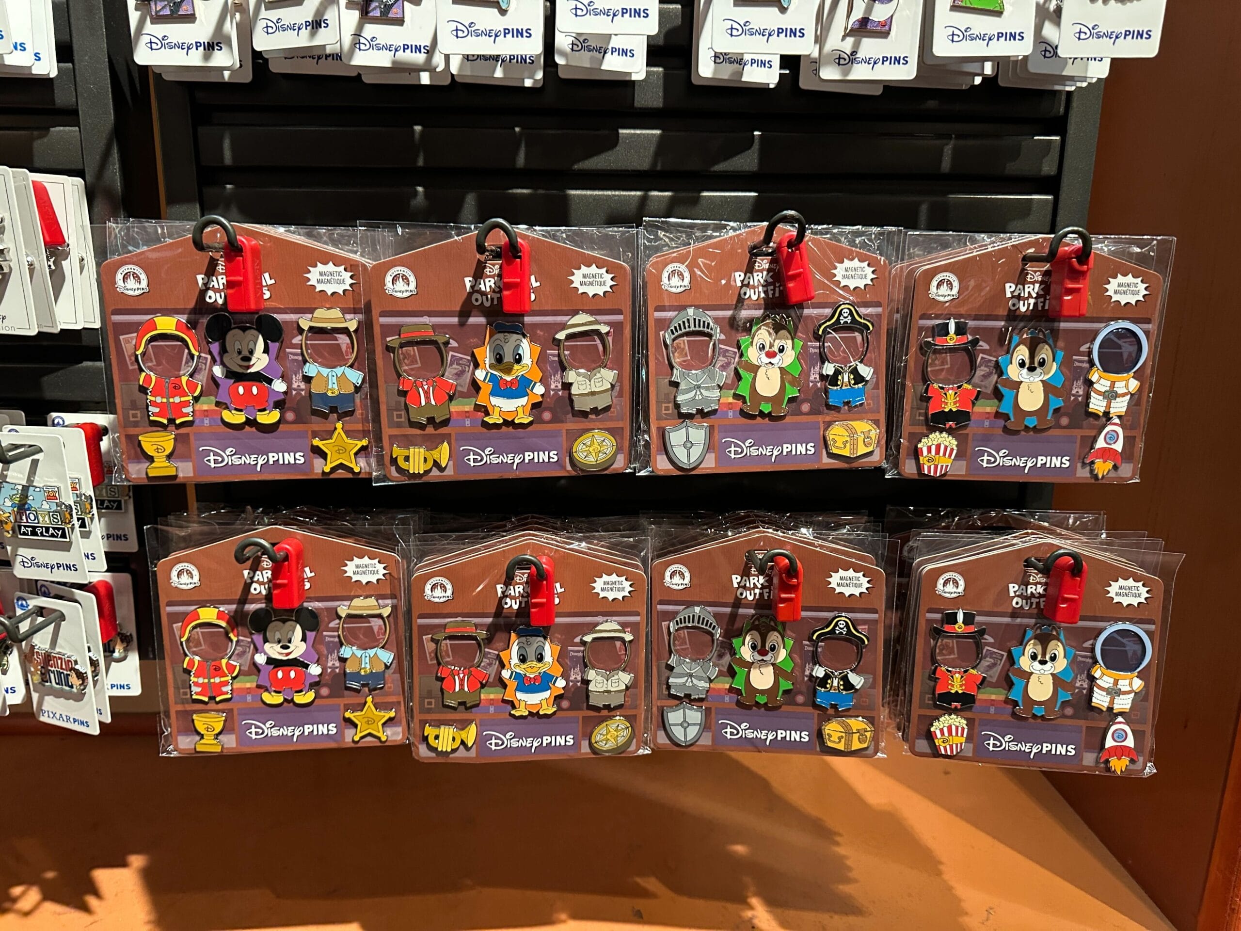 Disney pin sets featuring Mickey Mouse in various costumes are displayed on a store shelf.
