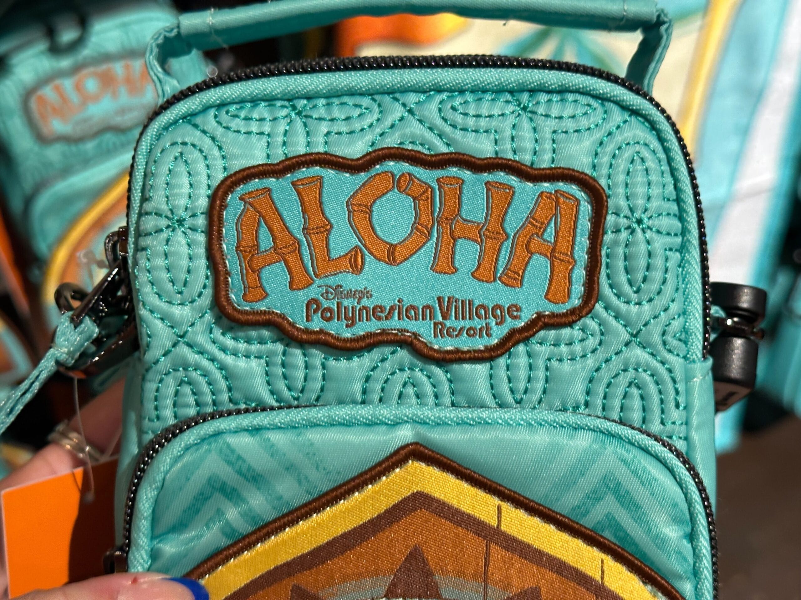 A teal bag with "ALOHA Disney's Polynesian Village Resort" embroidered in orange and brown letters.