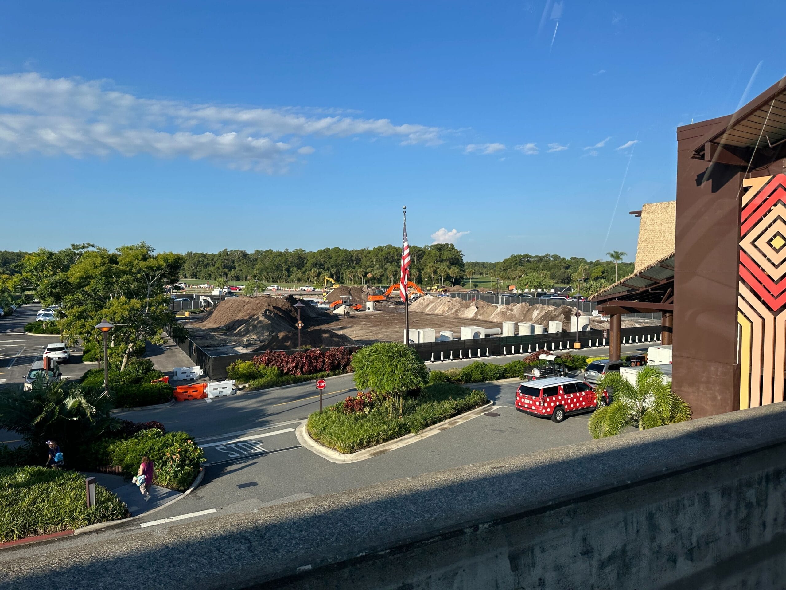 Construction site with piles of dirt and equipment near a parking lot and a building, under a clear blue sky at the Polynesian Resort.