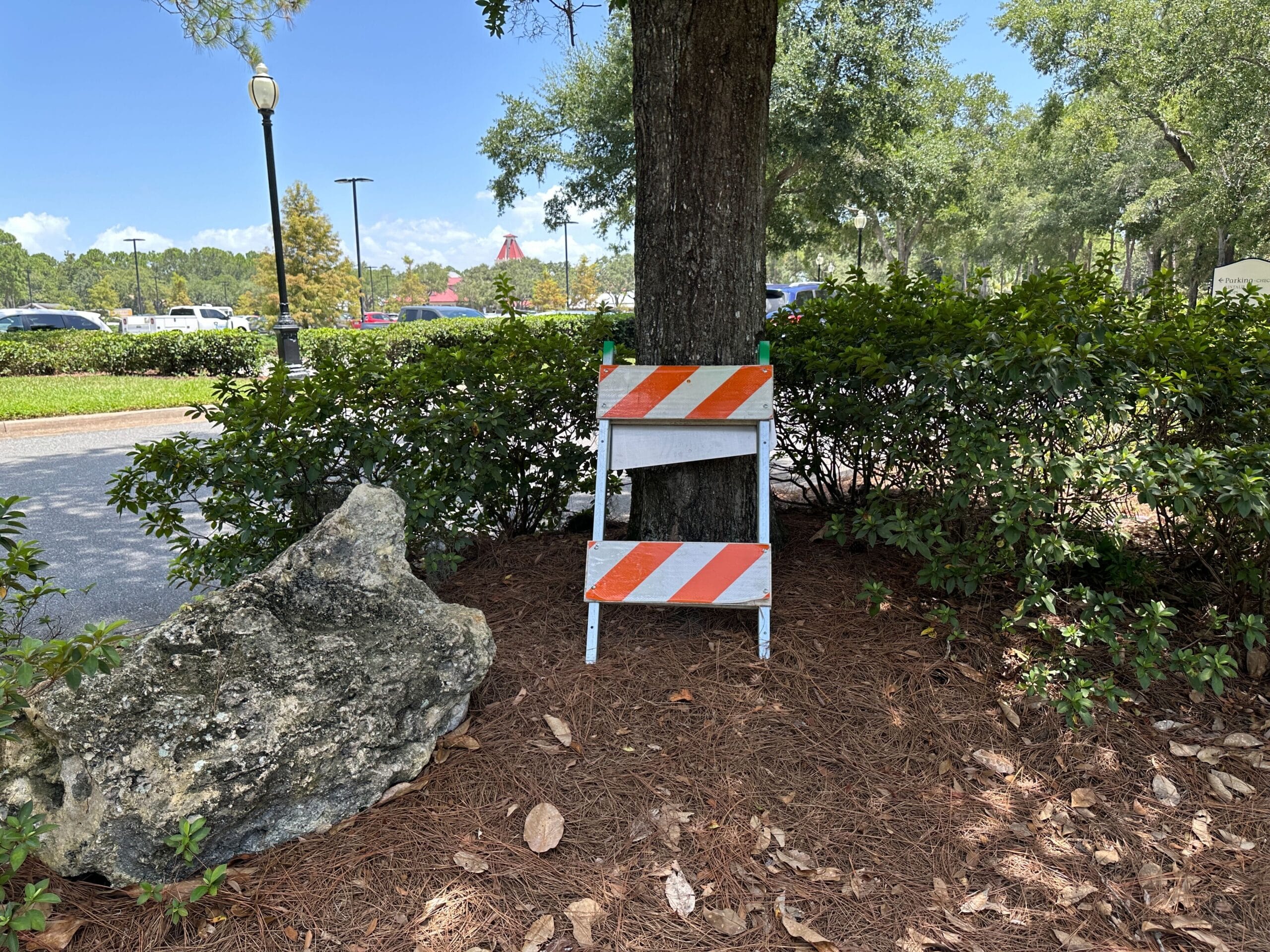 An orange and white striped road barrier stands near bushes by a parking lot at Disney’s Port Orleans Resort.
