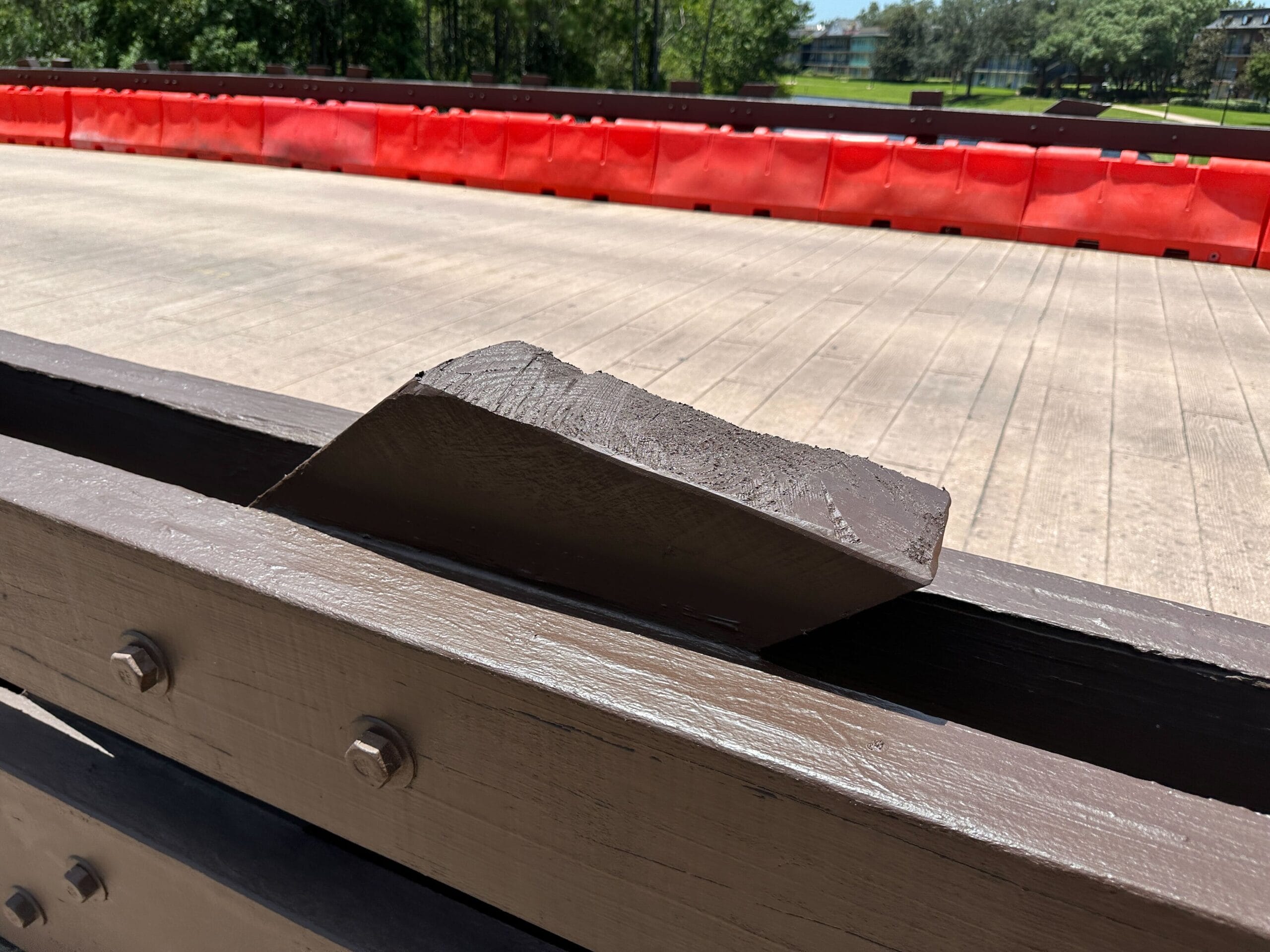 A large broken piece of brown wood rests on a wooden railing near a road after a truck accident.