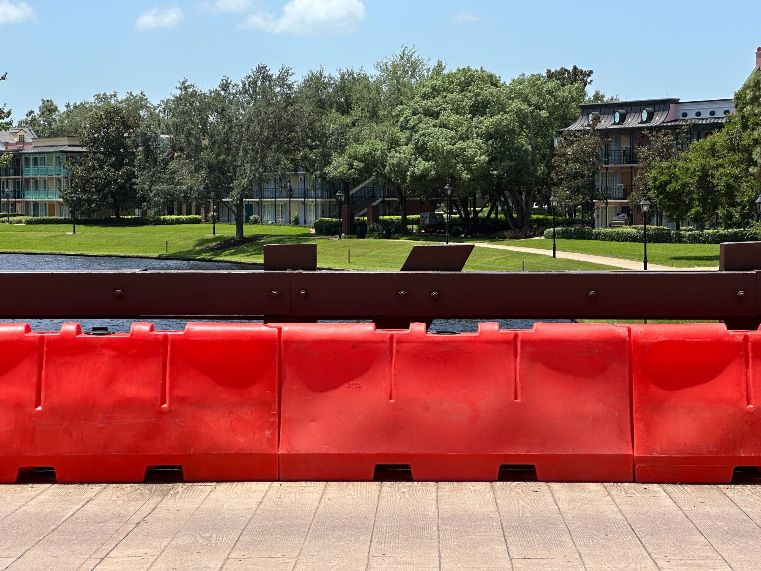 Bright red barricades on a wooden bridge at Disney’s Port Orleans Resort, trees and buildings in the background.