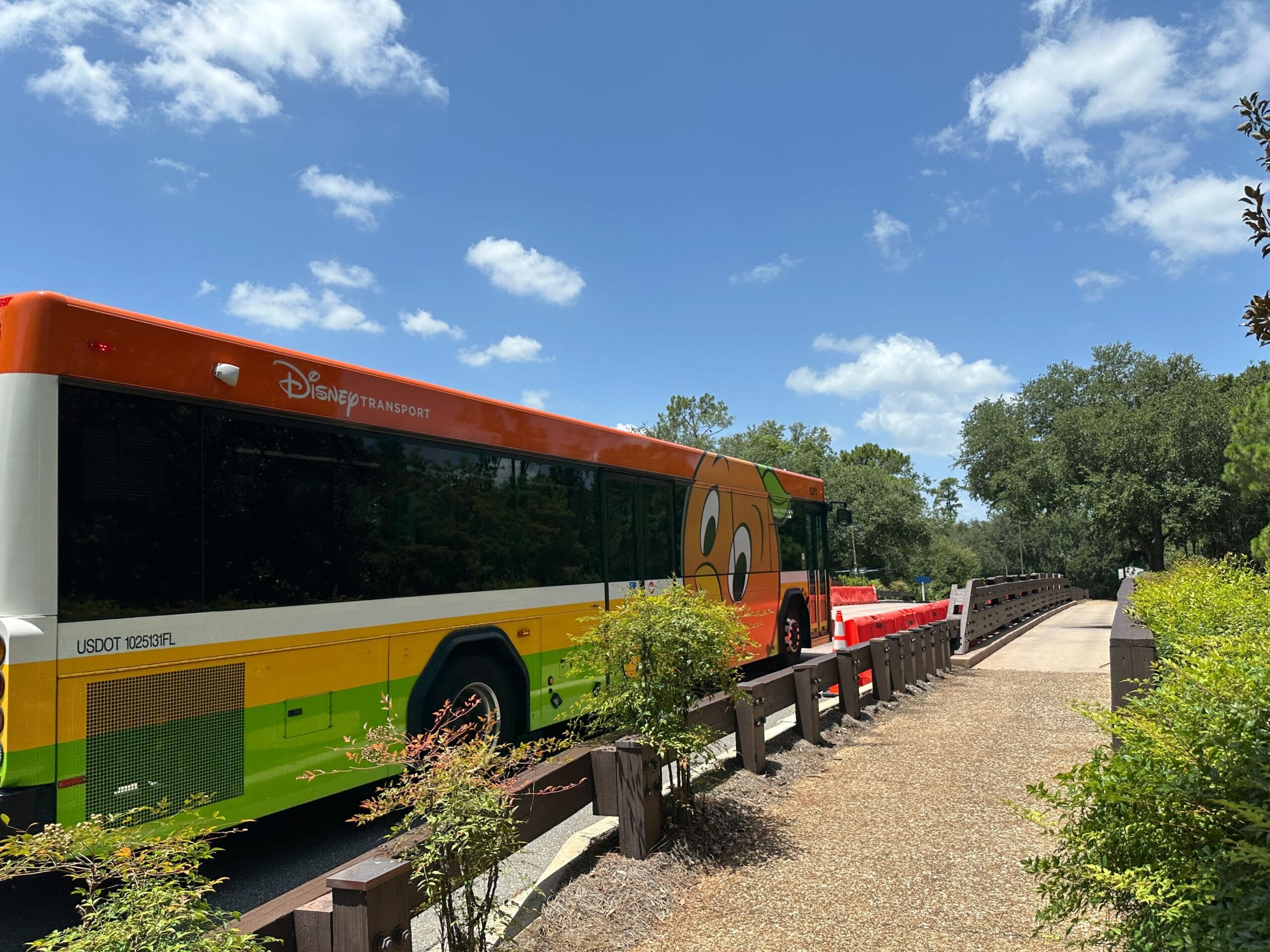 A Disney Transport bus with a cartoon Orange Bird character design is parked near Disney’s Port Orleans Resort on a sunny day.