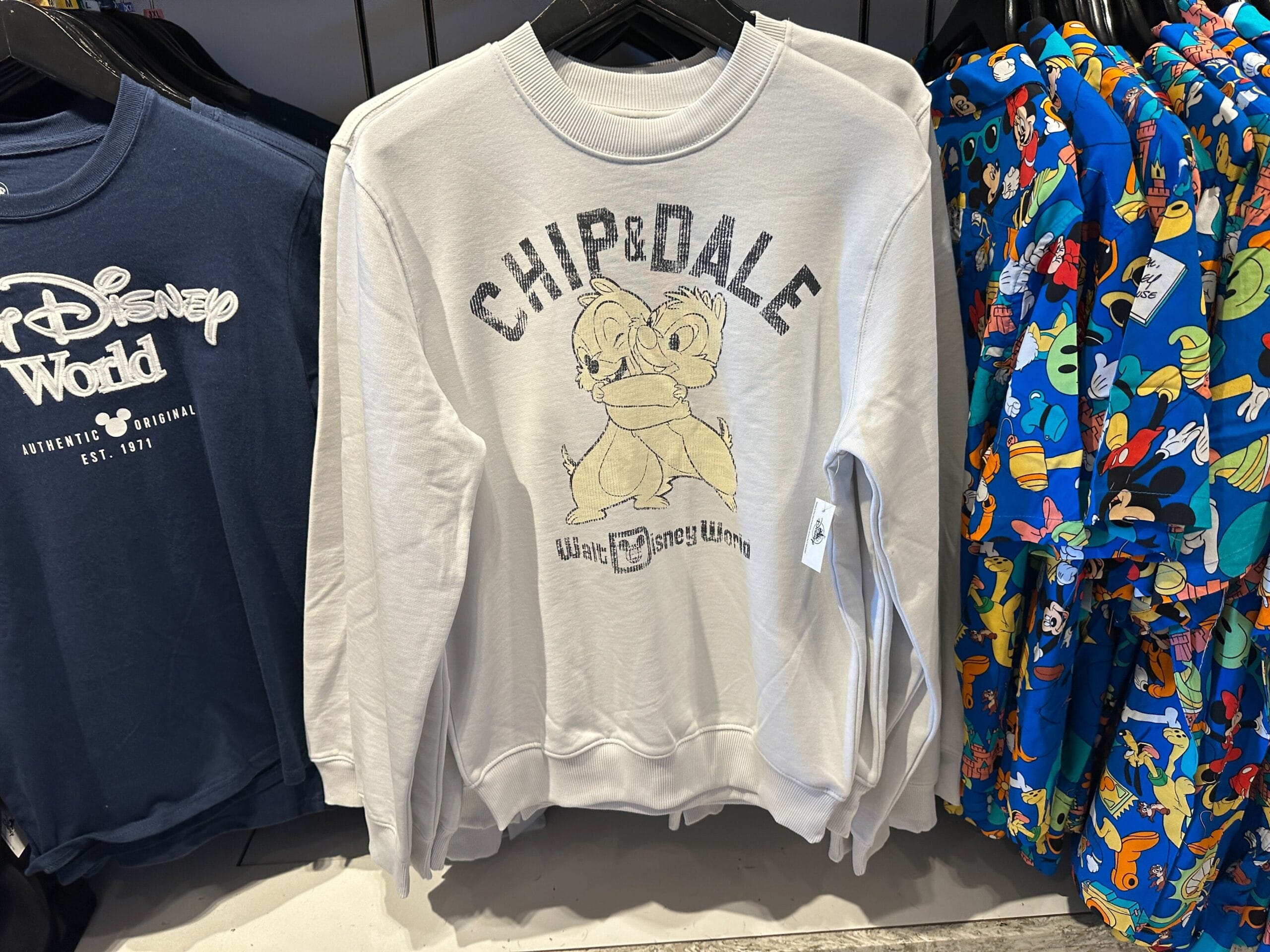 A white sweatshirt with Chip and Dale graphic hangs among Disney-themed shirts—a fun piece of new Disney products.