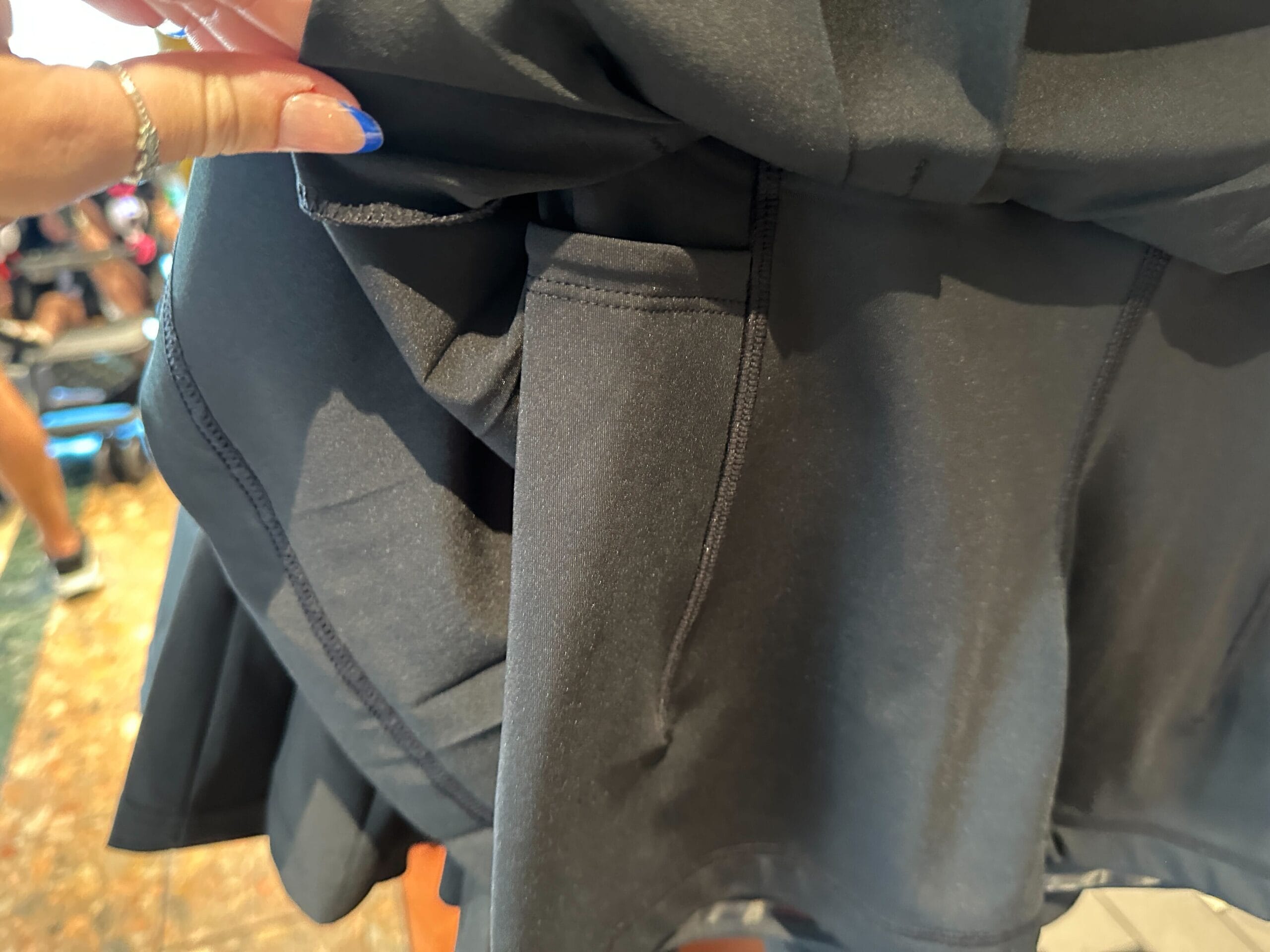 A hand holding black athletic shorts, highlighting a hidden pocket—perfect for stashing small Disney merchandise.