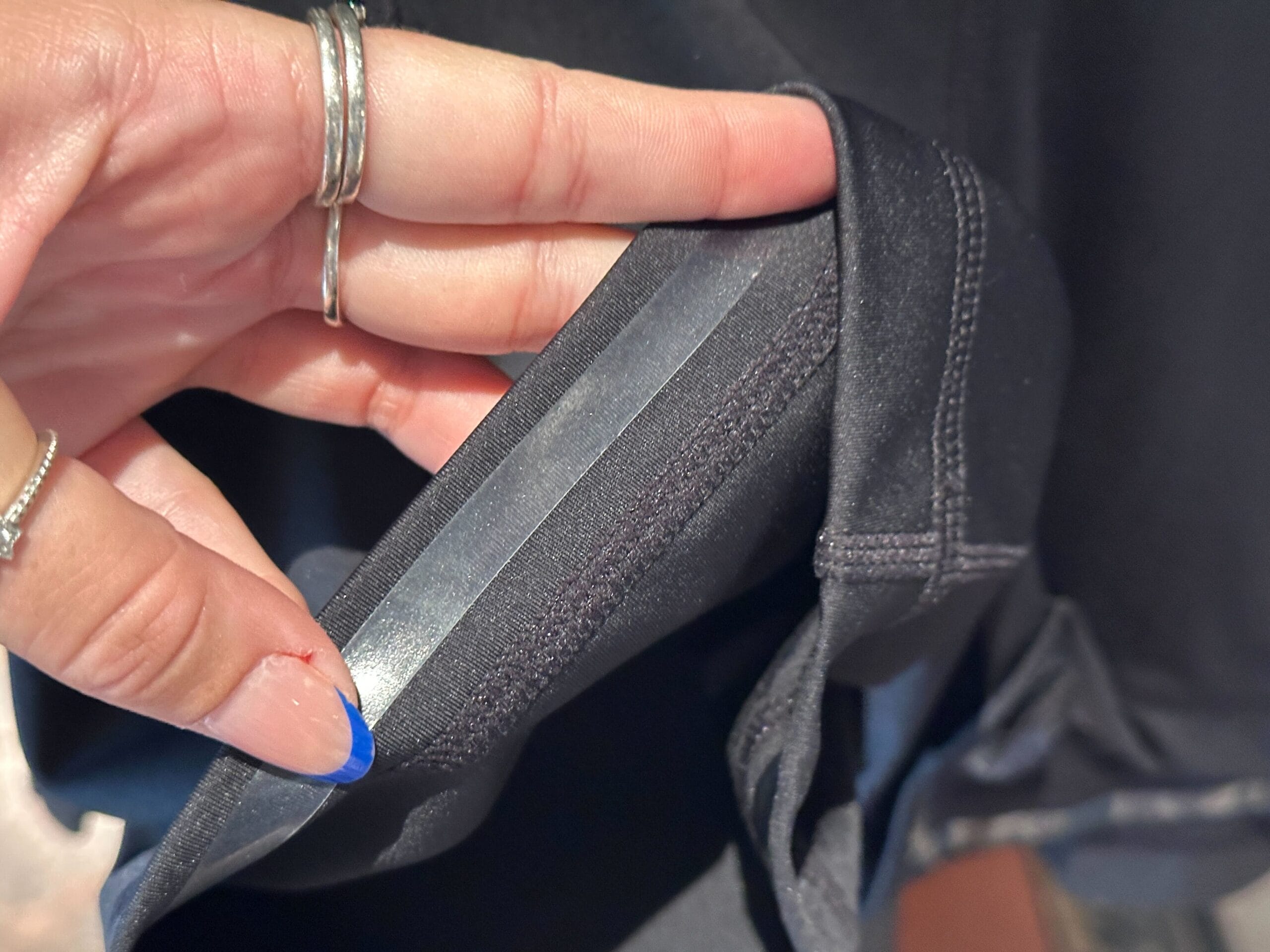 A hand with blue nail polish holds black fabric, showcasing a seam and adhesive tape—perfect for DIY Disney merchandise.