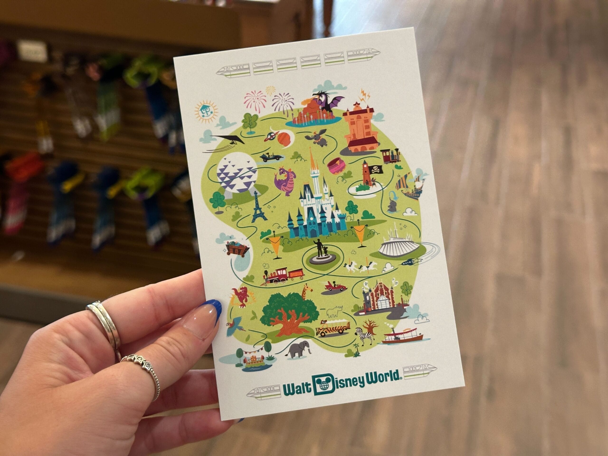 A hand holds a colorful Walt Disney World map postcard—perfect for fans of new Disney products and WDW merch.